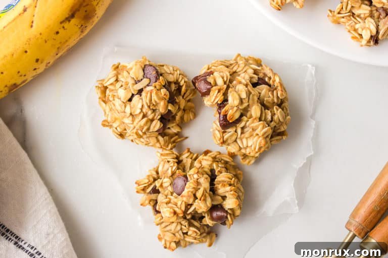 A trio of freshly baked banana oat cookies, perfectly golden and adorned with chocolate chips, rests on a delicate slip of wax paper.