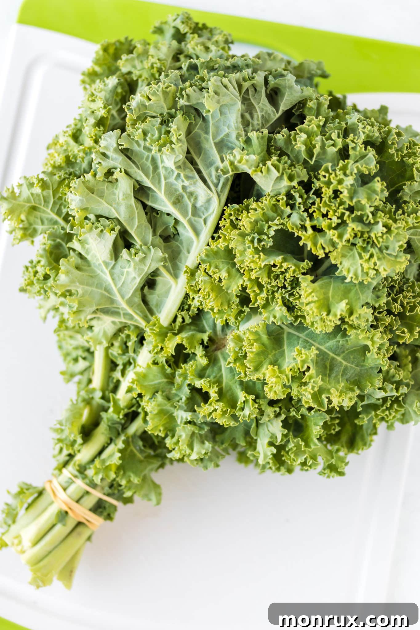 A bunch of vibrant green curly kale sits on a wooden cutting board, ready for preparation into crispy chips.