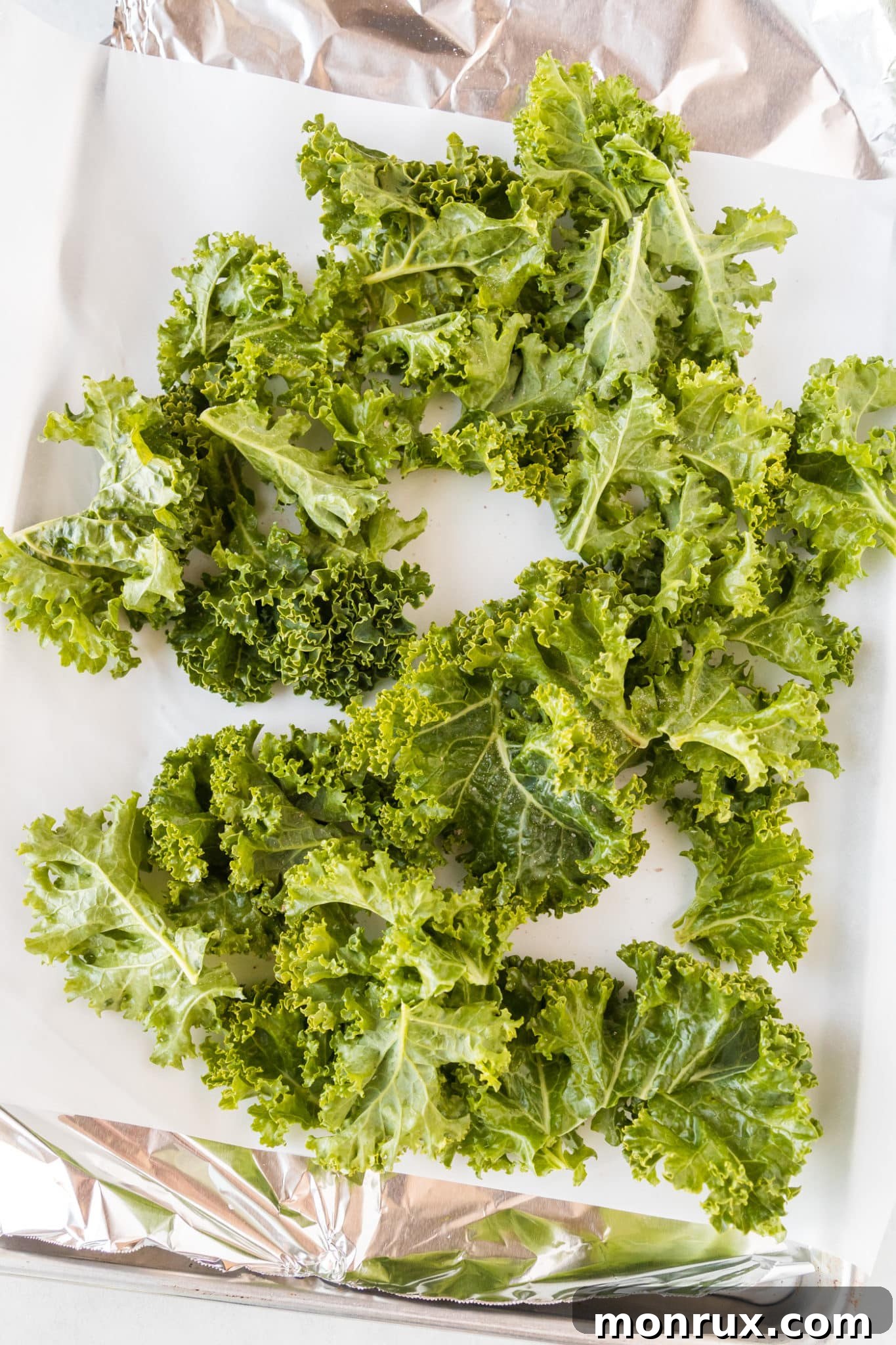 Crispy kale chips are evenly spread on a parchment-lined baking sheet, ready for oven baking.