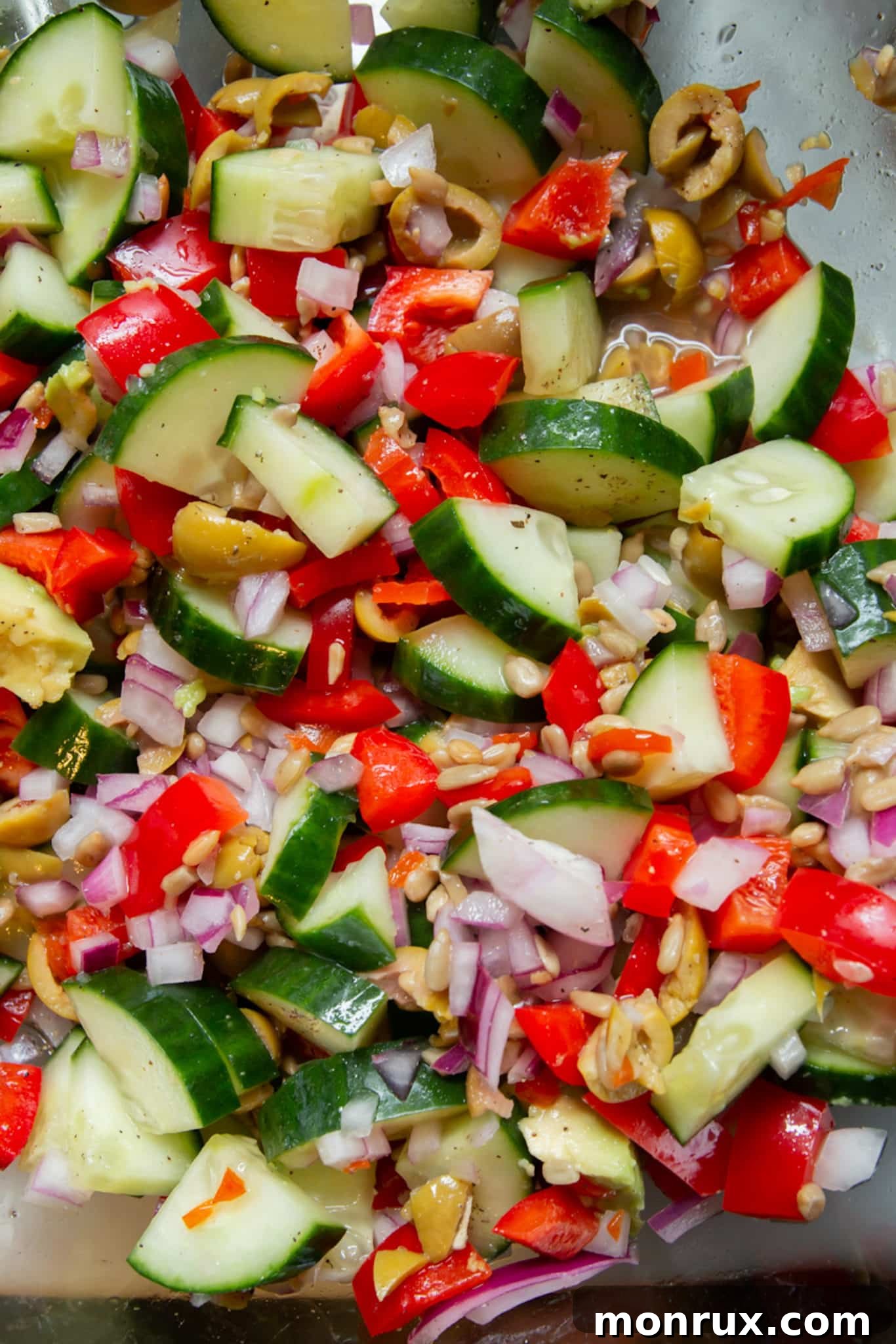 Close-up of chopped cucumbers, olives, and red onion being added to a bowl as part of a lentil salad preparation.