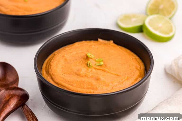 A beautifully presented bowl of creamy peanut butter soup in a dark bowl, garnished with fresh herbs, ready to be served. The rich texture and inviting color highlight the comforting nature of the dish.