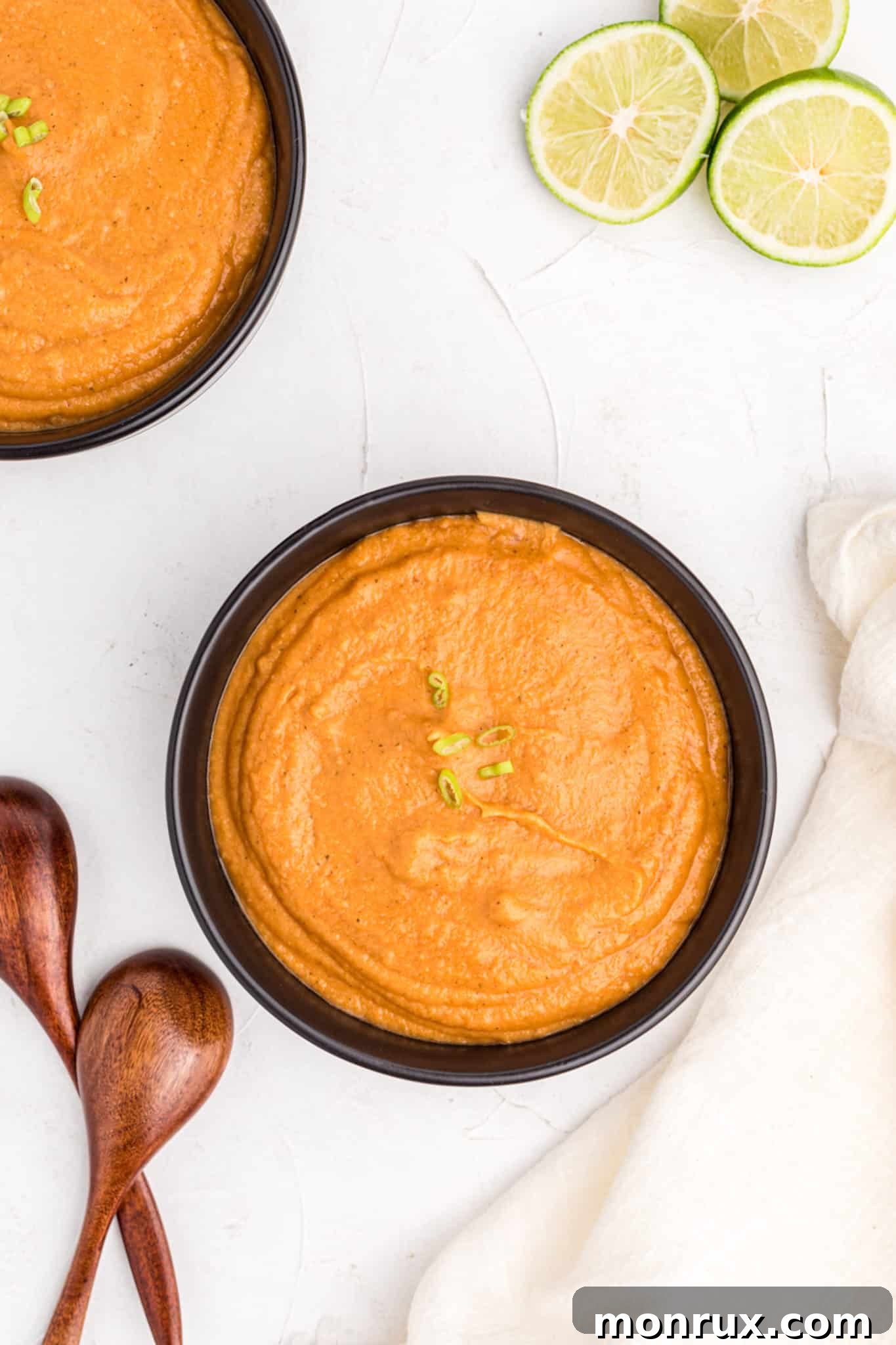 Two bowls of creamy peanut butter soup, garnished with fresh herbs and a swirl of coconut milk, set on a dark table, radiating warmth and inviting comfort.
