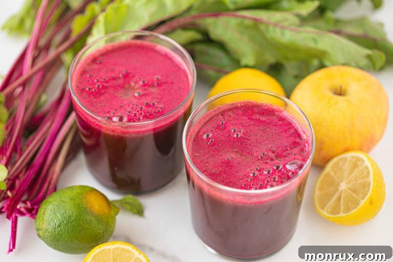 two glasses of homemade beet juice surrounded by lemons and beet greens.