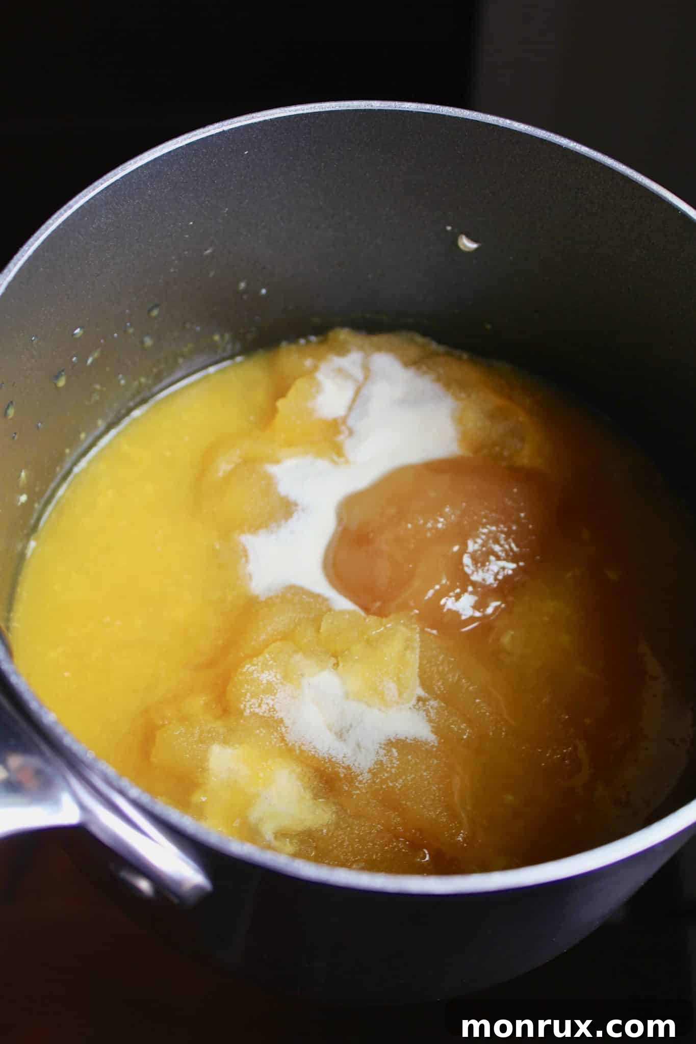 A medium saucepan on a stovetop, containing the orange juice, sweetener, and gelatin mixture, being whisked to combine.