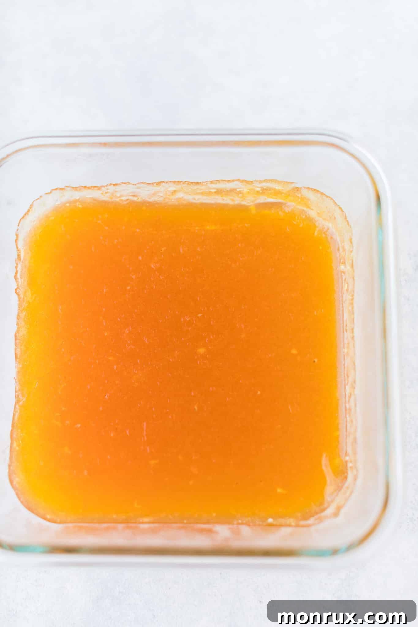Homemade orange jello mixture poured into a glass baking dish, cooling before setting.