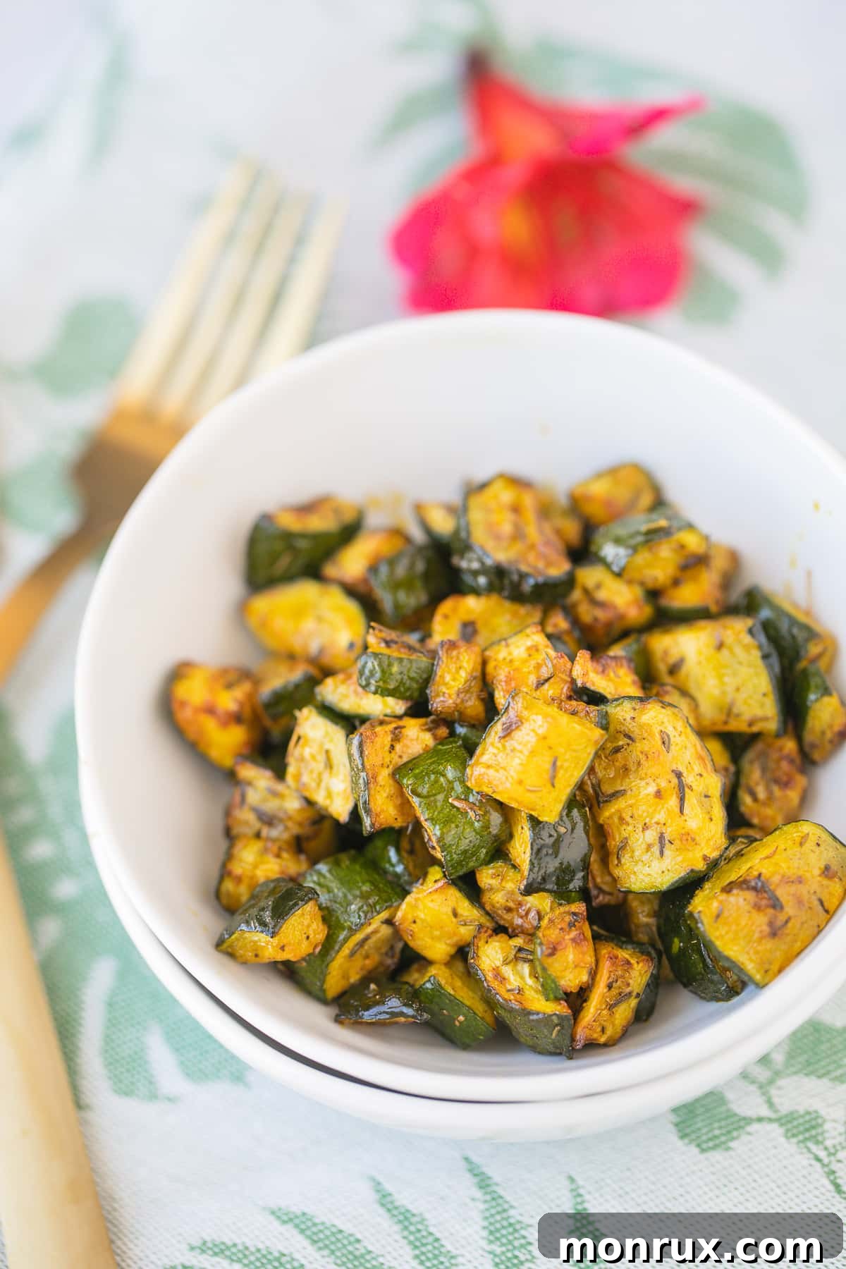 red palm oil roasted zucchini in a white bowl with gold forks