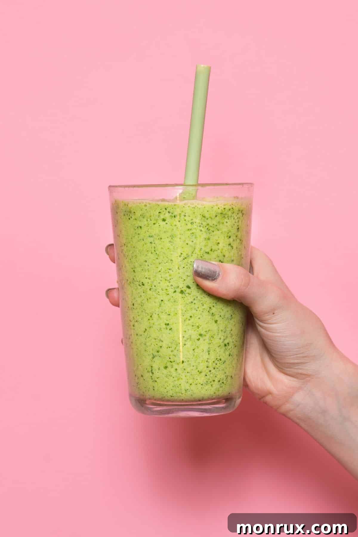woman holding a green smoothie in front of a pink background.