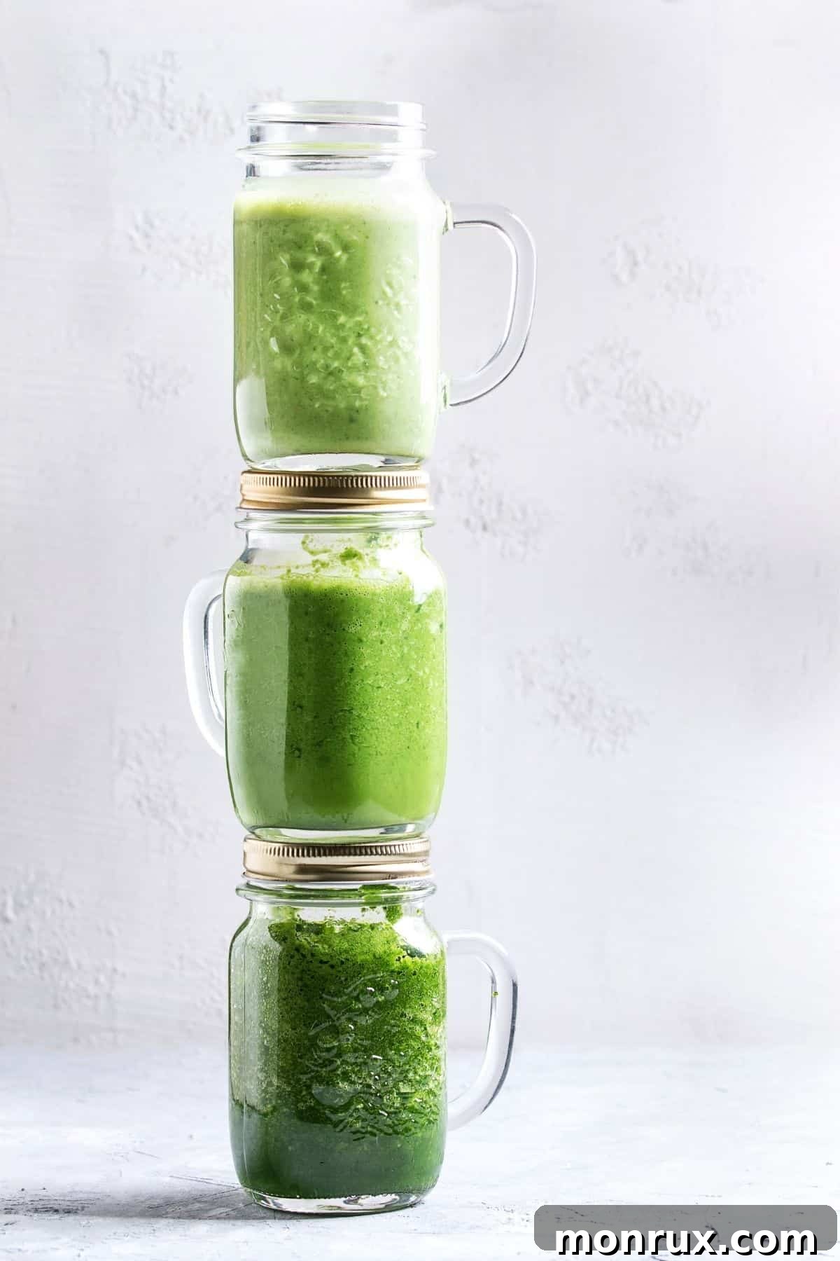three jars of green smoothies stack on top of each other.