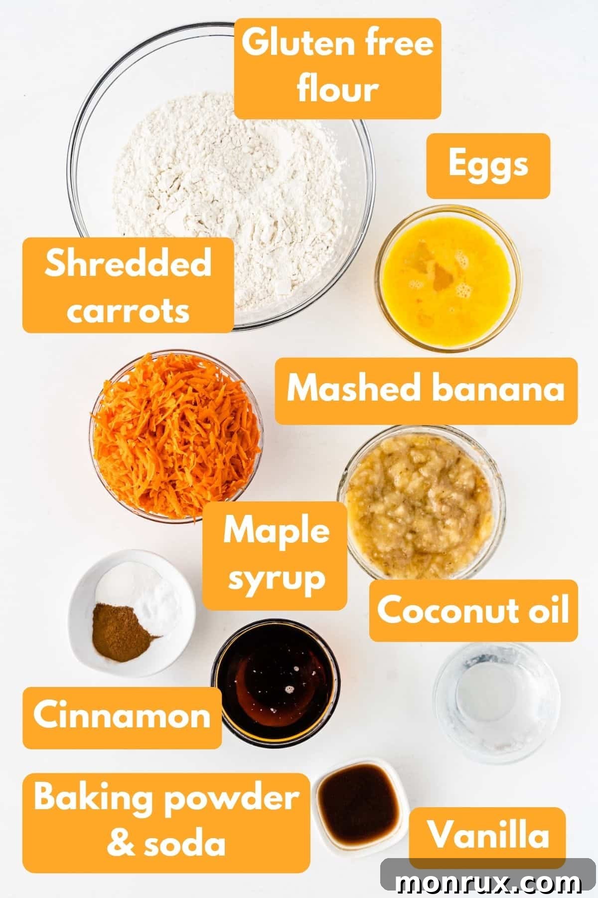 A flat lay of fresh ingredients laid out on a wooden surface, including bananas, carrots, flour, eggs, and maple syrup, essential for making banana carrot muffins.