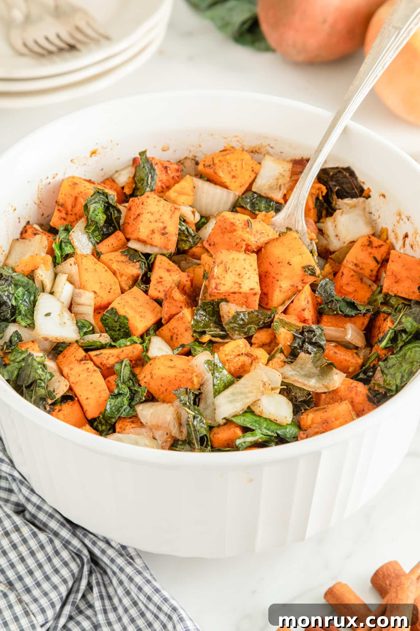 Large white ceramic bowl filled with baked kale and sweet potatoes, plus onion.