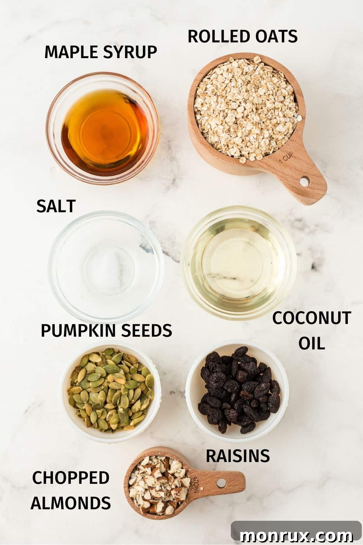 A collection of raw ingredients laid out on a surface, including rolled oats, almonds, pumpkin seeds, raisins, and a small bowl of maple syrup and coconut oil, ready for making homemade granola.