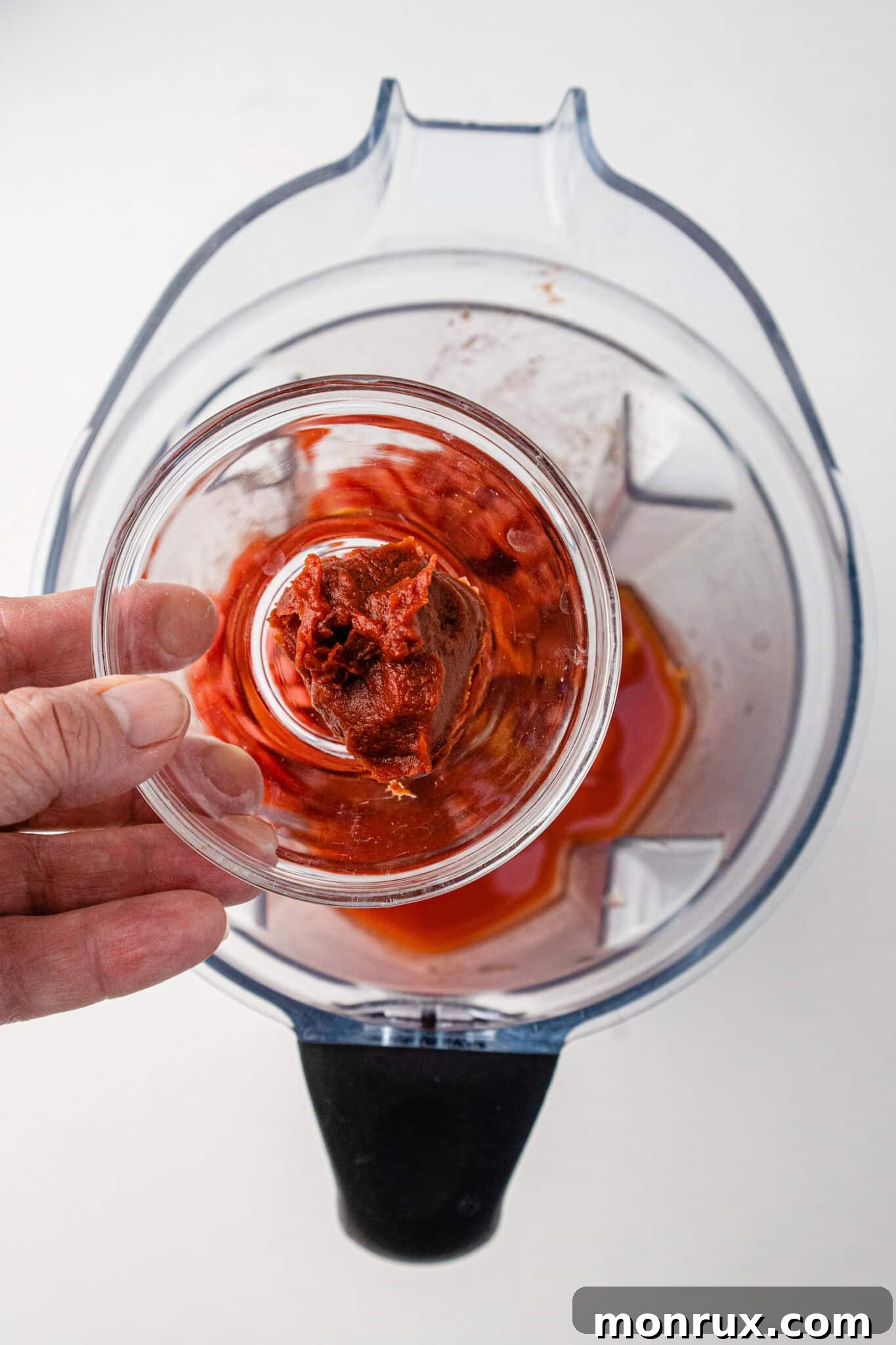 A spoon adding tomato paste to the diced tomatoes in the blender.