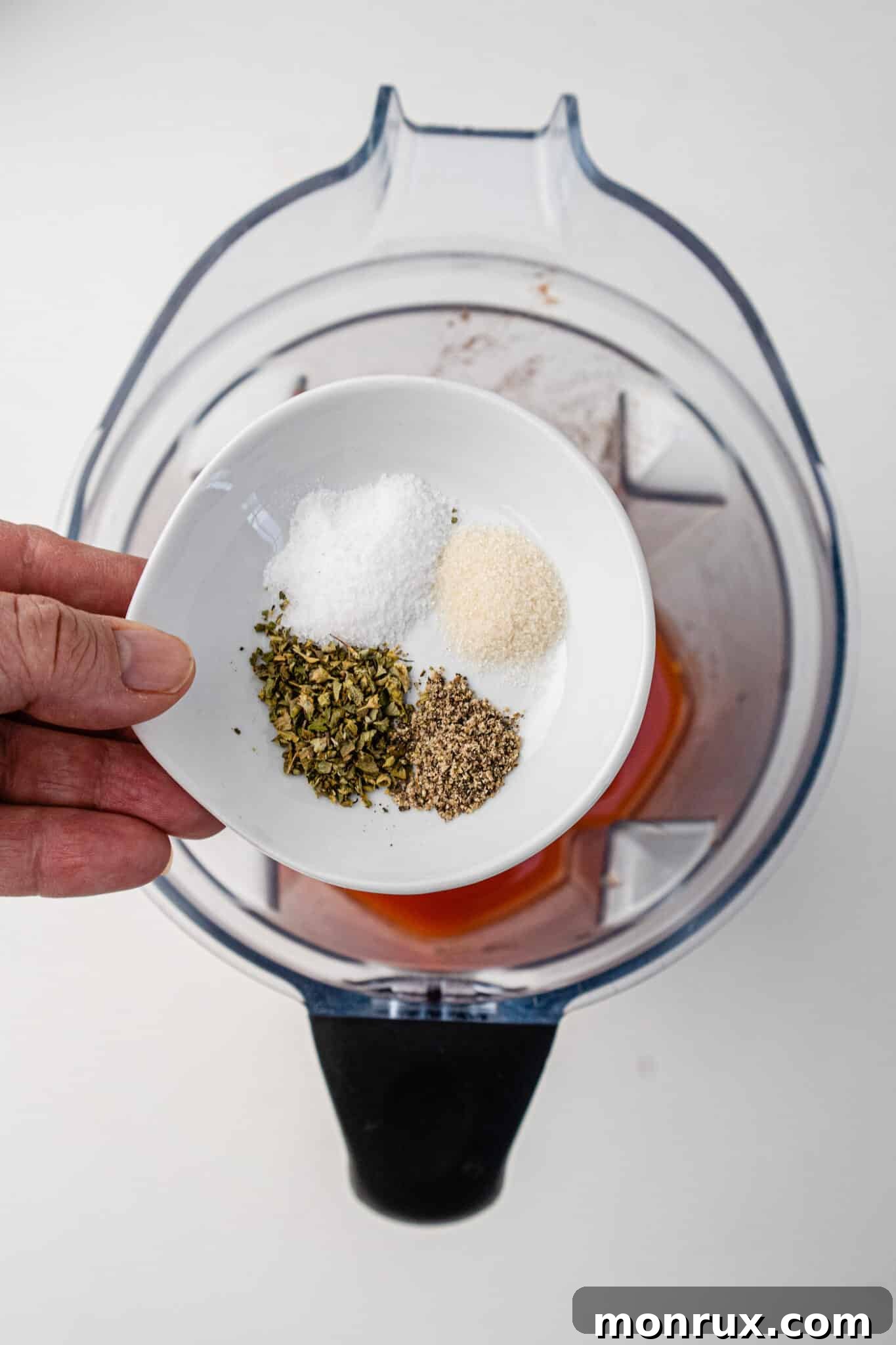 Various seasonings being sprinkled into the Vitamix with tomatoes and tomato paste.