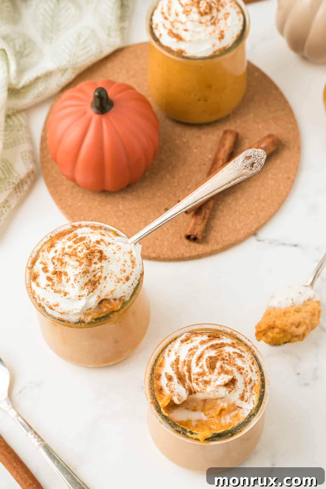 A charming place setting featuring individual jars of healthy pumpkin pudding, topped with coconut whipped cream and a sprinkle of cinnamon, perfect for holiday serving.