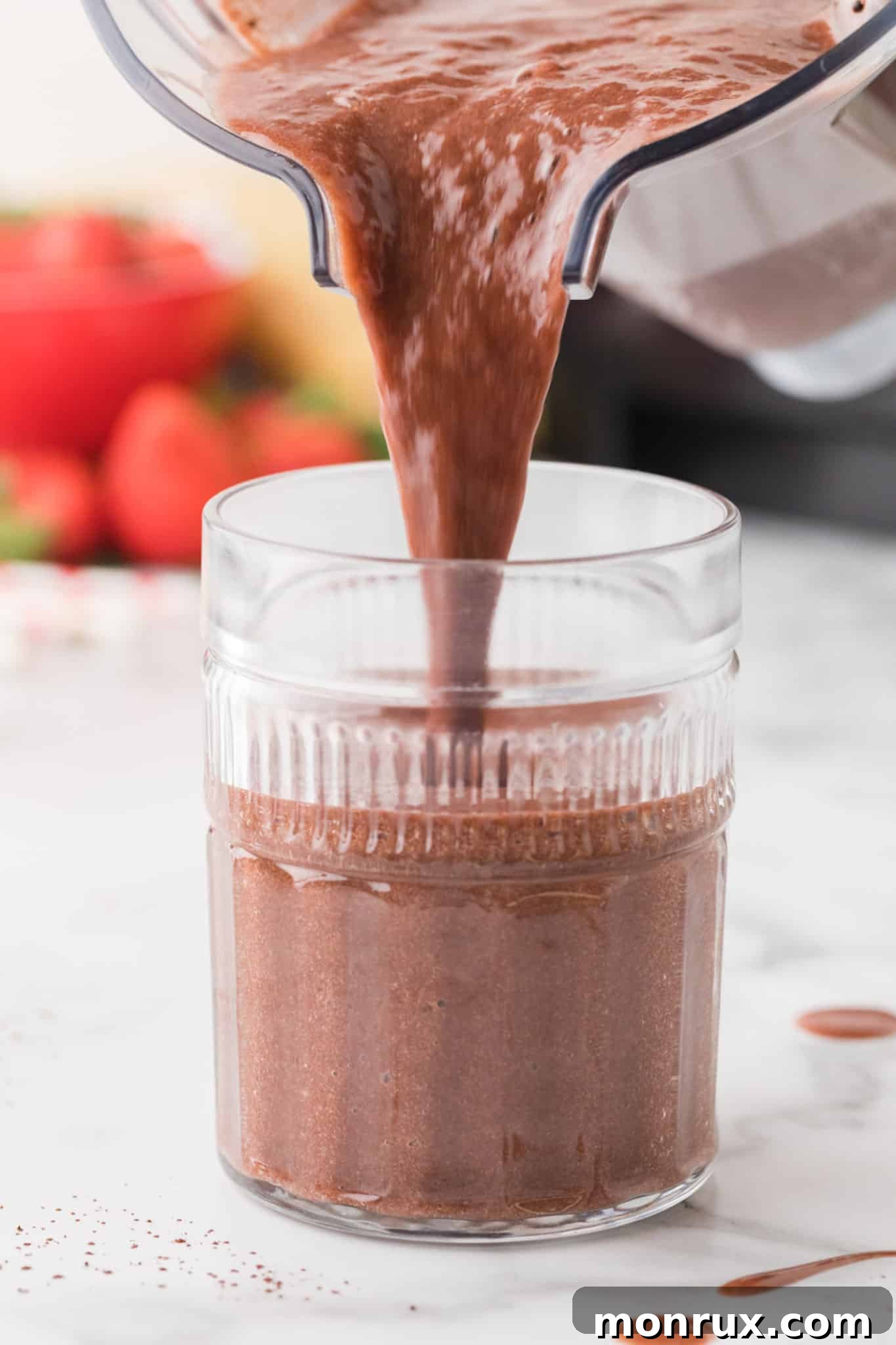 Freshly blended strawberry banana chocolate smoothie being poured from the blender into a serving glass, ready to enjoy.