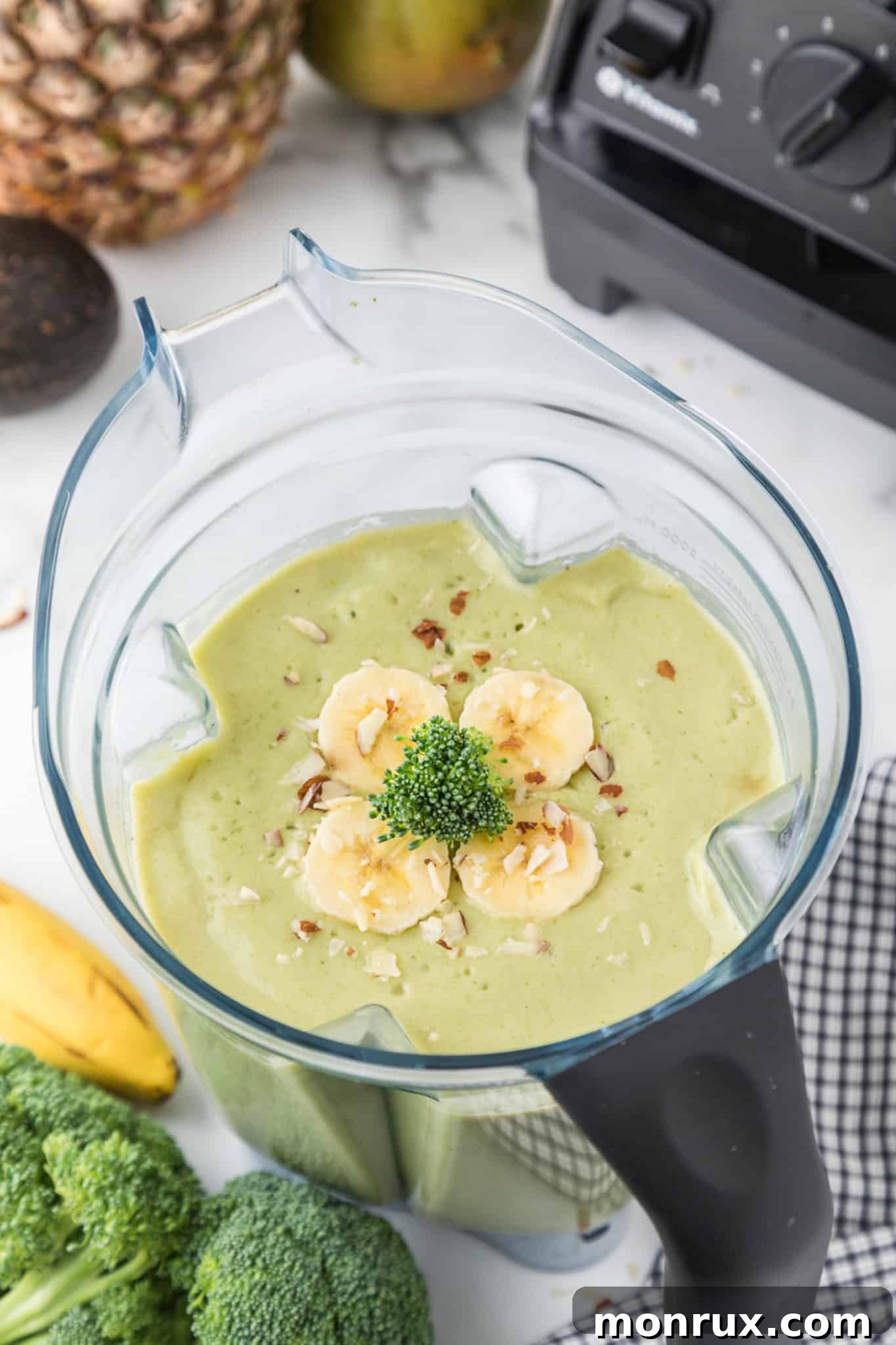 A vibrant green broccoli pineapple smoothie in a glass blender, ready to be poured, showcasing fresh ingredients.