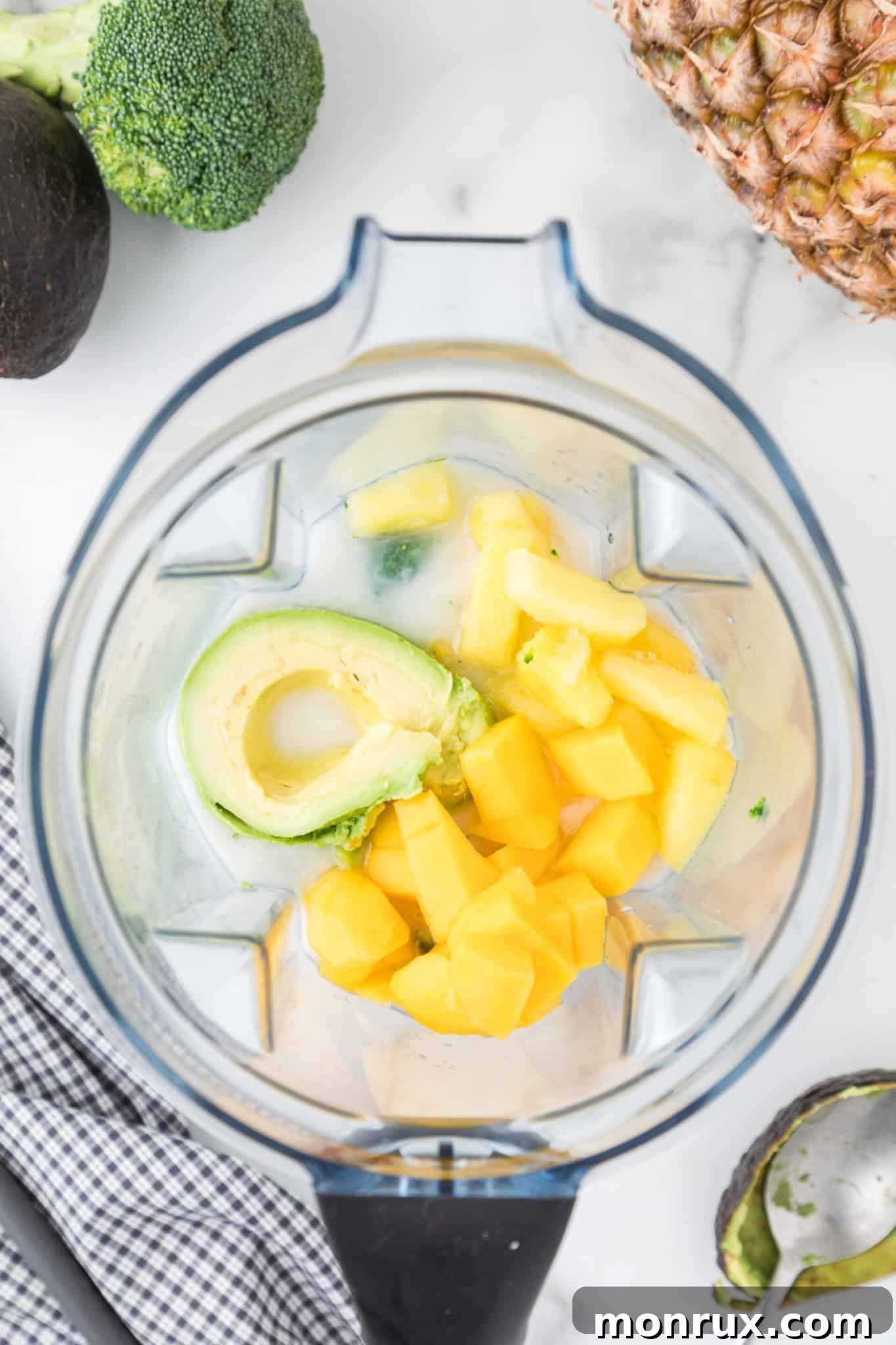 Close-up of broccoli, pineapple, banana, and avocado in a high-speed Vitamix blender, ready for blending.