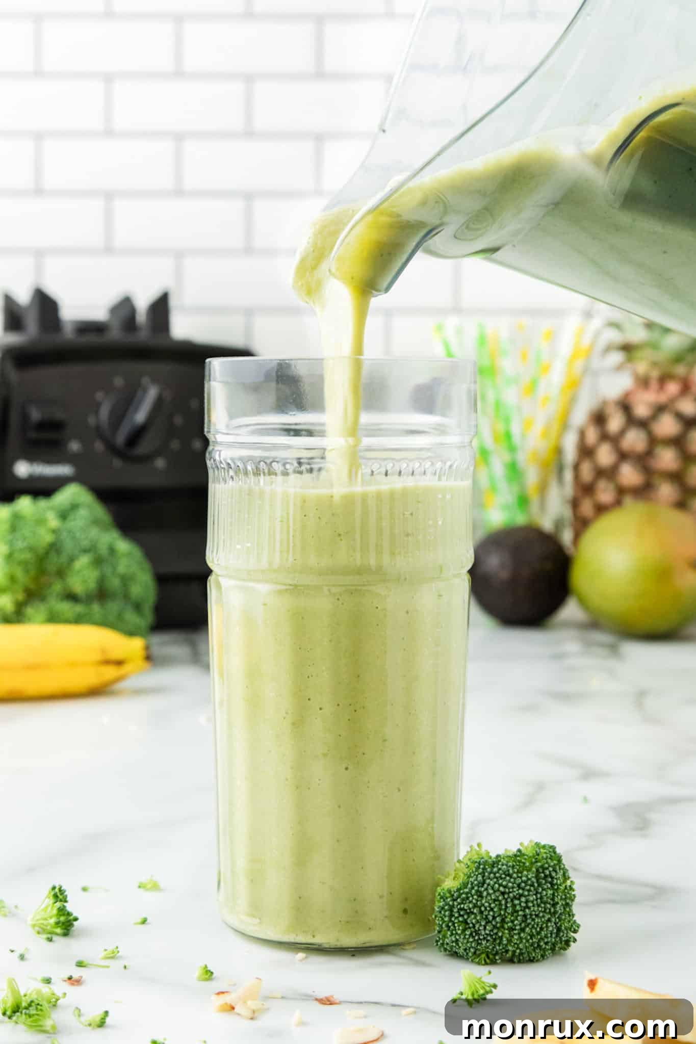 A vibrant green broccoli pineapple smoothie being poured from a blender into a clear glass, creating a delicious stream.