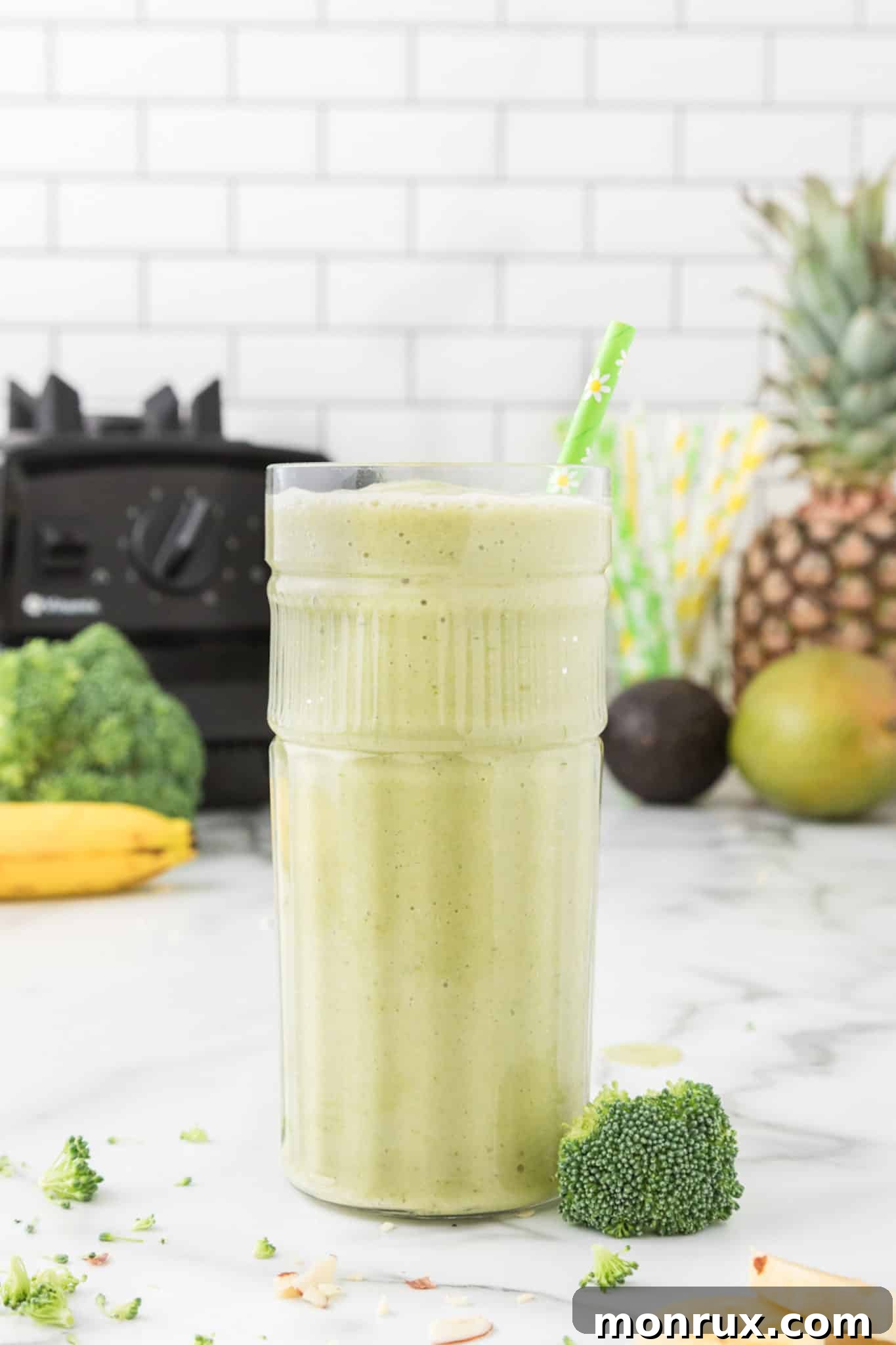 A refreshing glass of green broccoli smoothie with a reusable straw, sitting on a clean kitchen countertop.