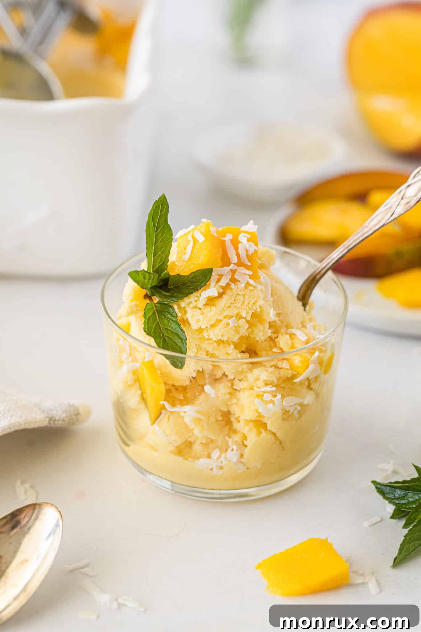 A bowl of vibrant vegan mango ice cream, garnished with fresh mint, ready to be enjoyed. A spoon rests in the bowl.