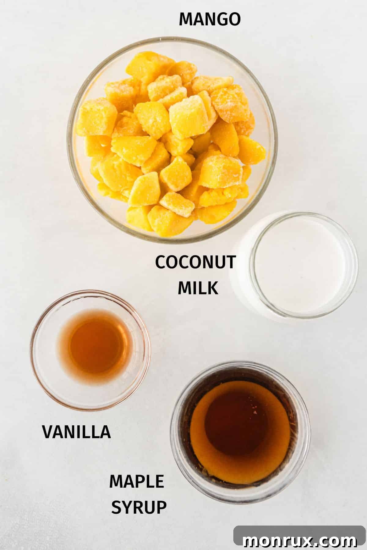 A flat lay photograph showcasing the four simple ingredients needed for mango ice cream: canned coconut milk, vanilla extract, frozen mango chunks, and maple syrup.