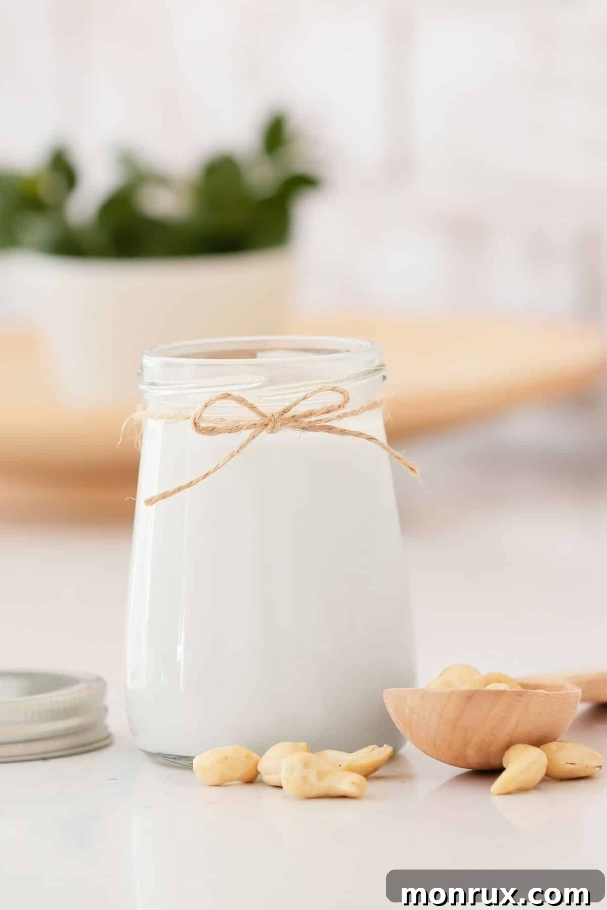 A glass of homemade cashew milk with a rustic string tied around the neck of the jar, sitting on a wooden surface.