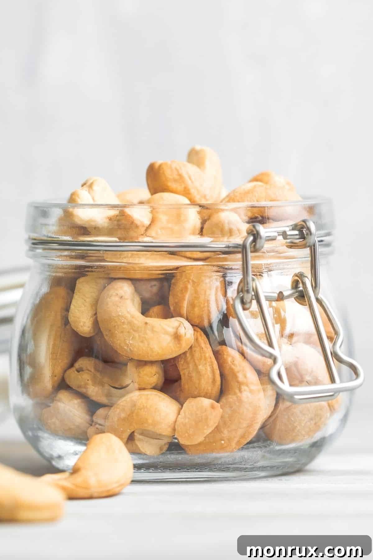 A glass jar filled with raw cashew nuts sitting on a wooden tabletop, ready for making milk.