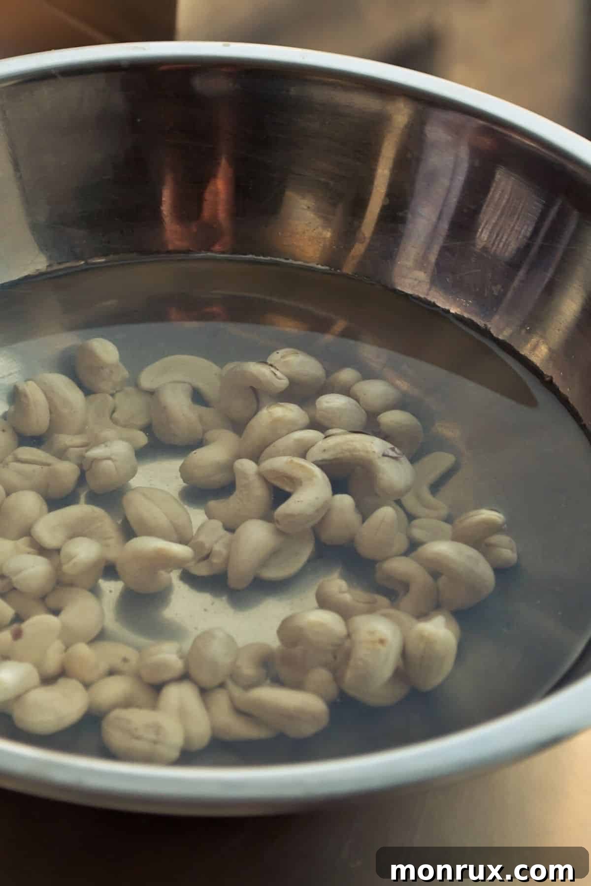 Raw cashews soaking in a clear bowl with filtered water, preparing them for blending.