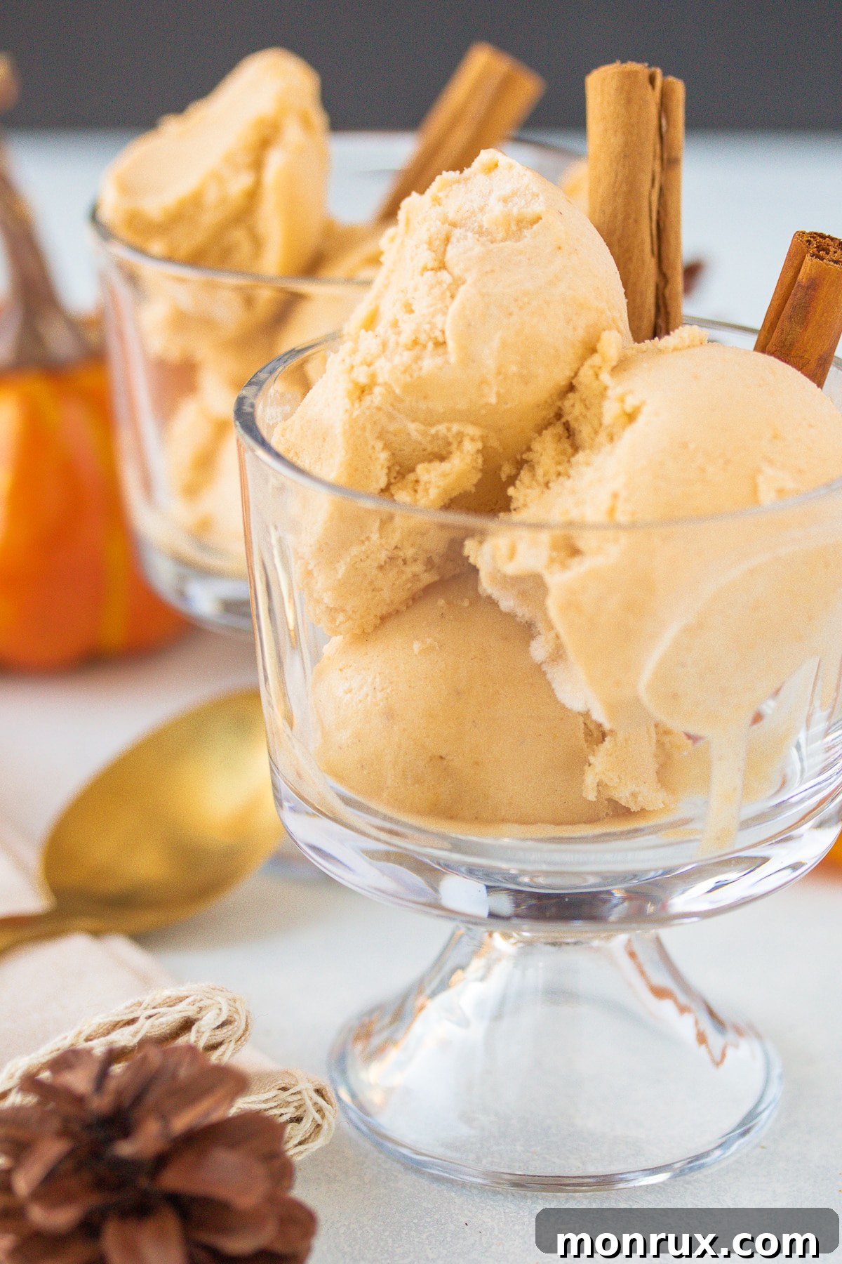 Two parfait glasses filled with vegan pumpkin ice cream and topped with dairy-free whipped cream.