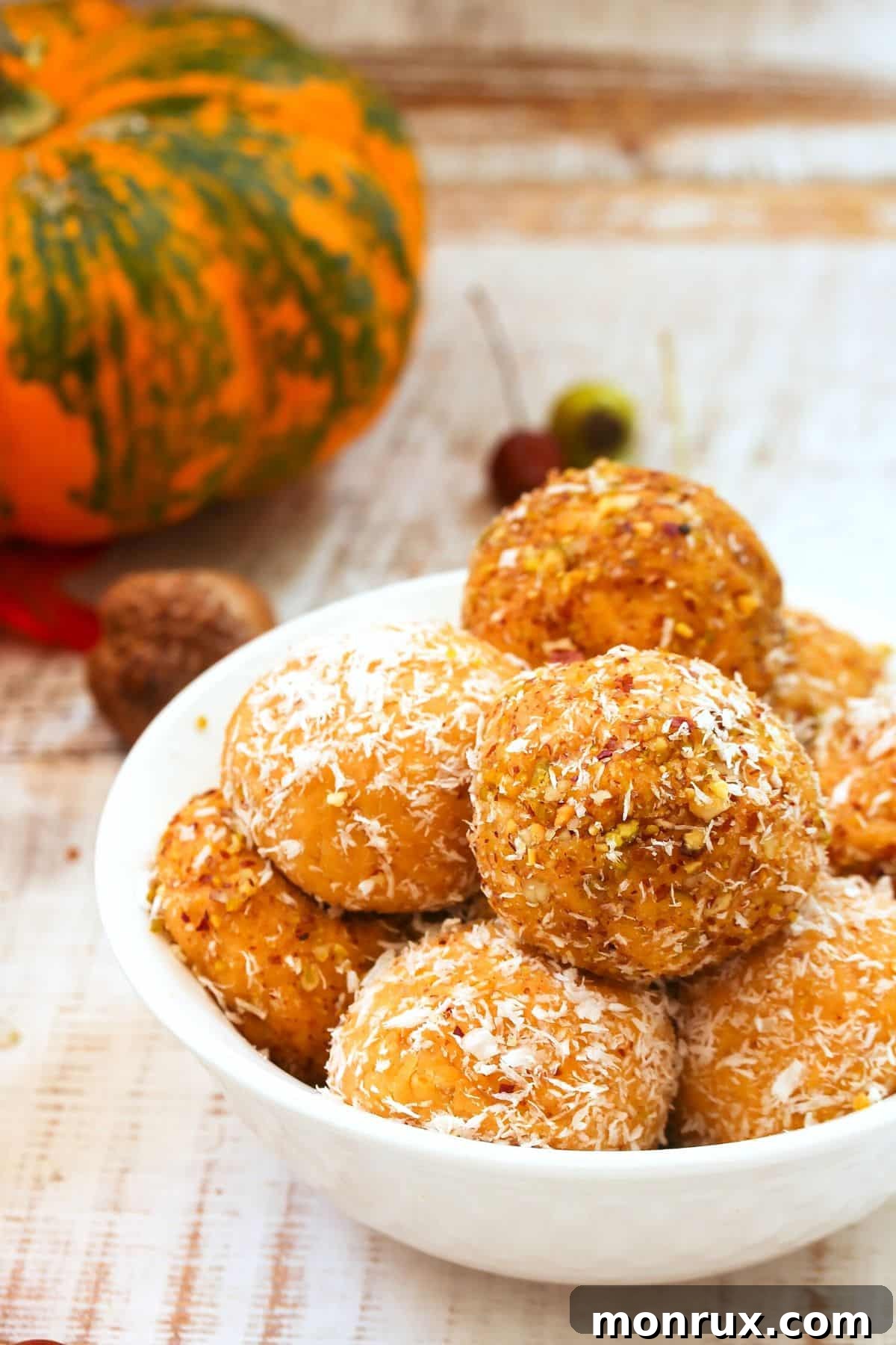 Up-close photo of vibrant orange pumpkin protein balls in a bowl, coated with shredded coconut and ready to eat.