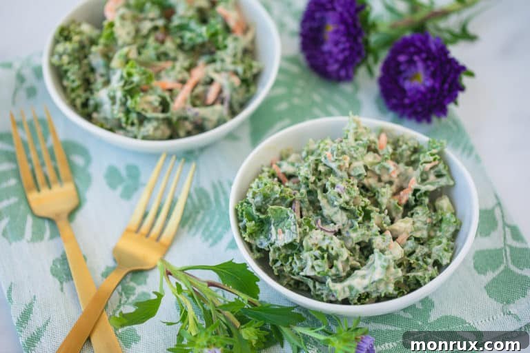 Two aesthetically arranged bowls of creamy kale salad, accompanied by gold forks and fresh purple flowers, enhancing the visual appeal of the dish.