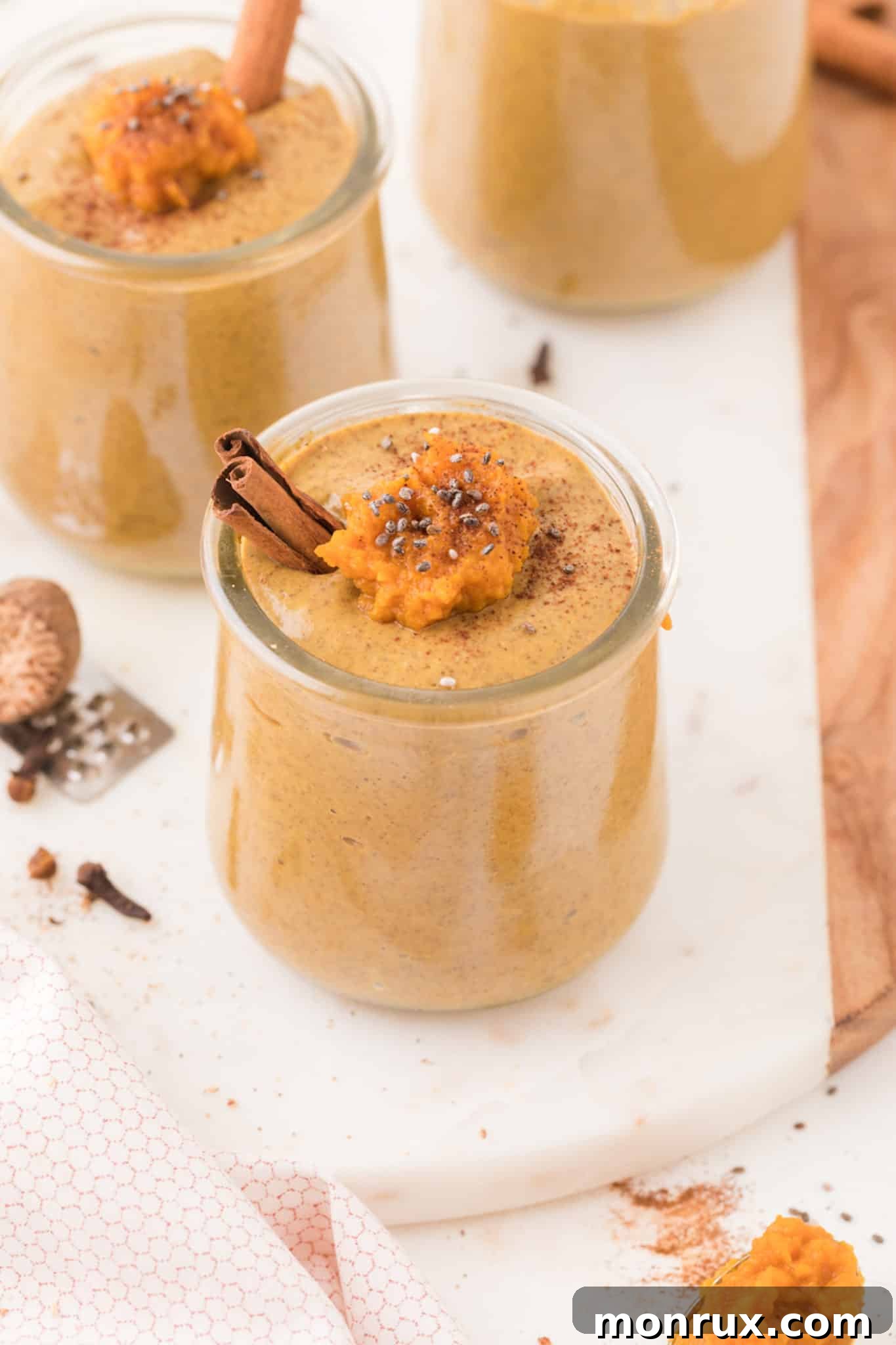Two glass jars filled with creamy pumpkin chia seed pudding, garnished with pumpkin seeds and a sprinkle of spice, set on a rustic wooden table.