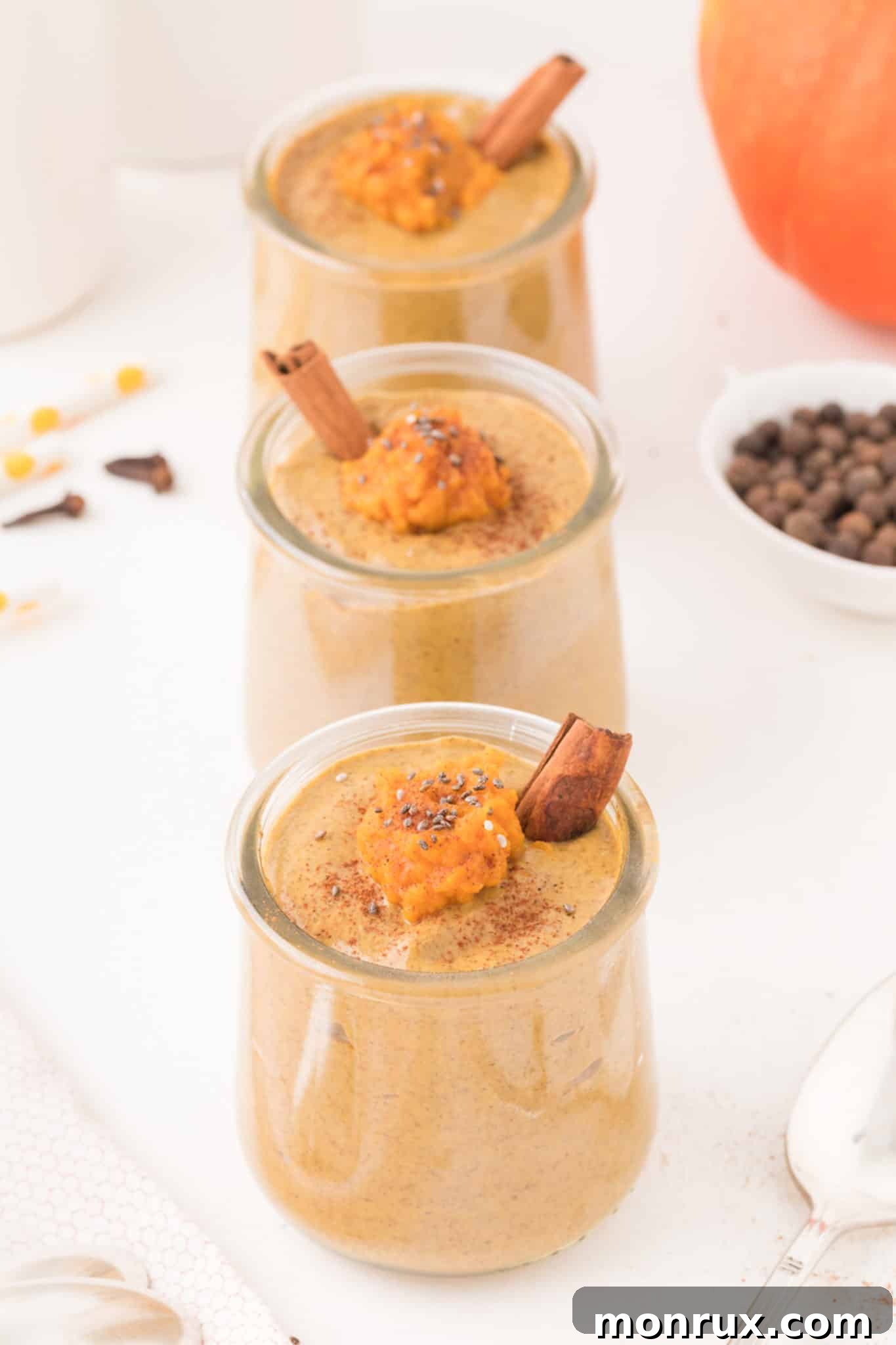 Three beautifully arranged glass jars of prepared pumpkin chia pudding, ready for serving.