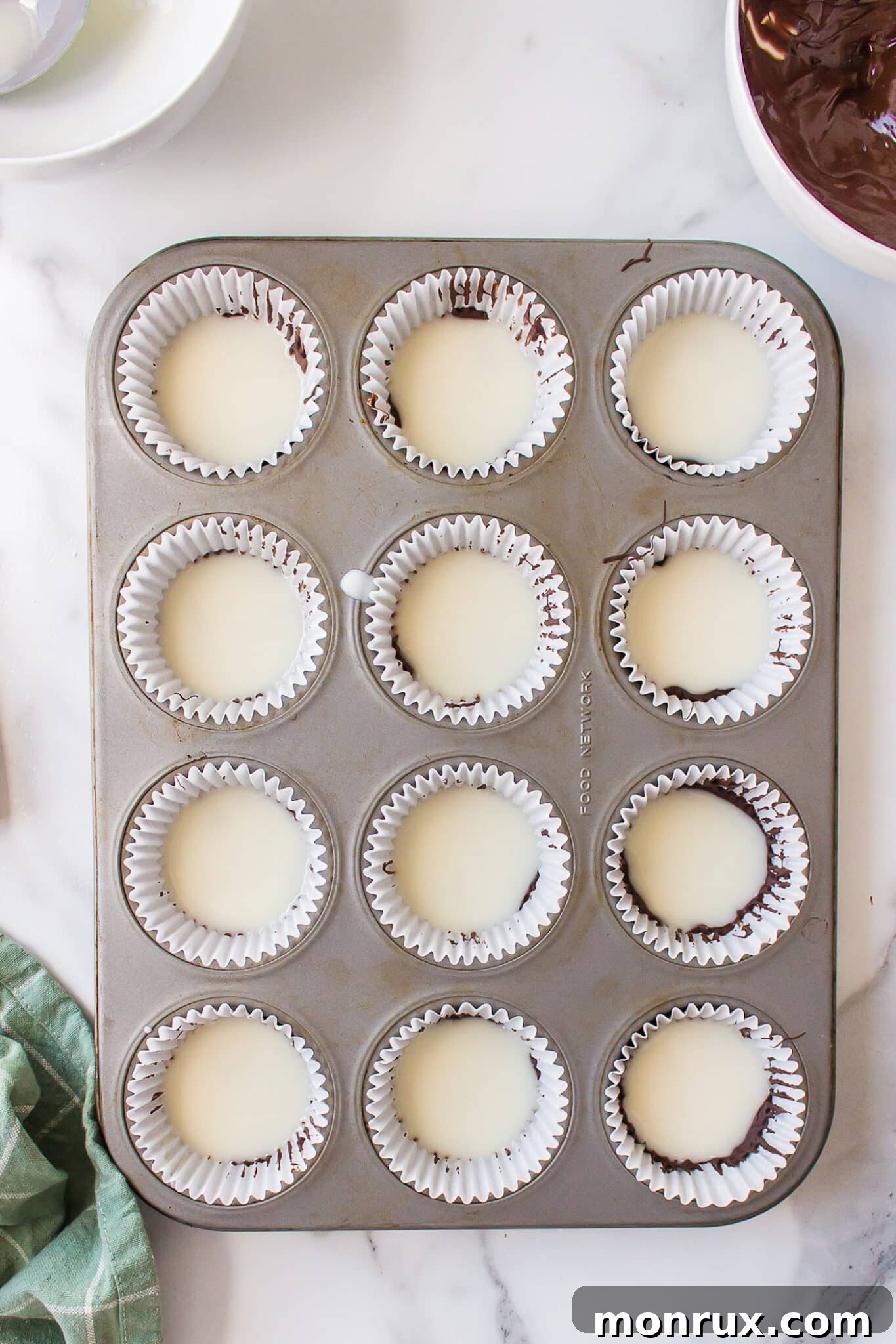 A layer of creamy coconut butter being spread over hardened chocolate for homemade peppermint patties.