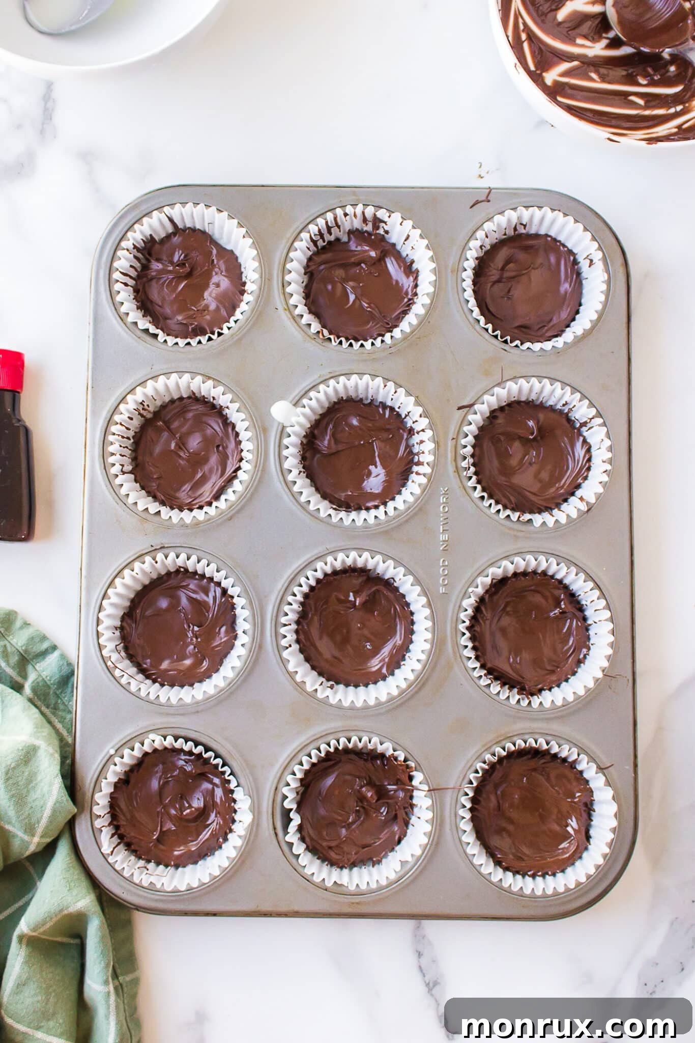 The final layer of melted chocolate being added to homemade peppermint patties in a muffin tin.