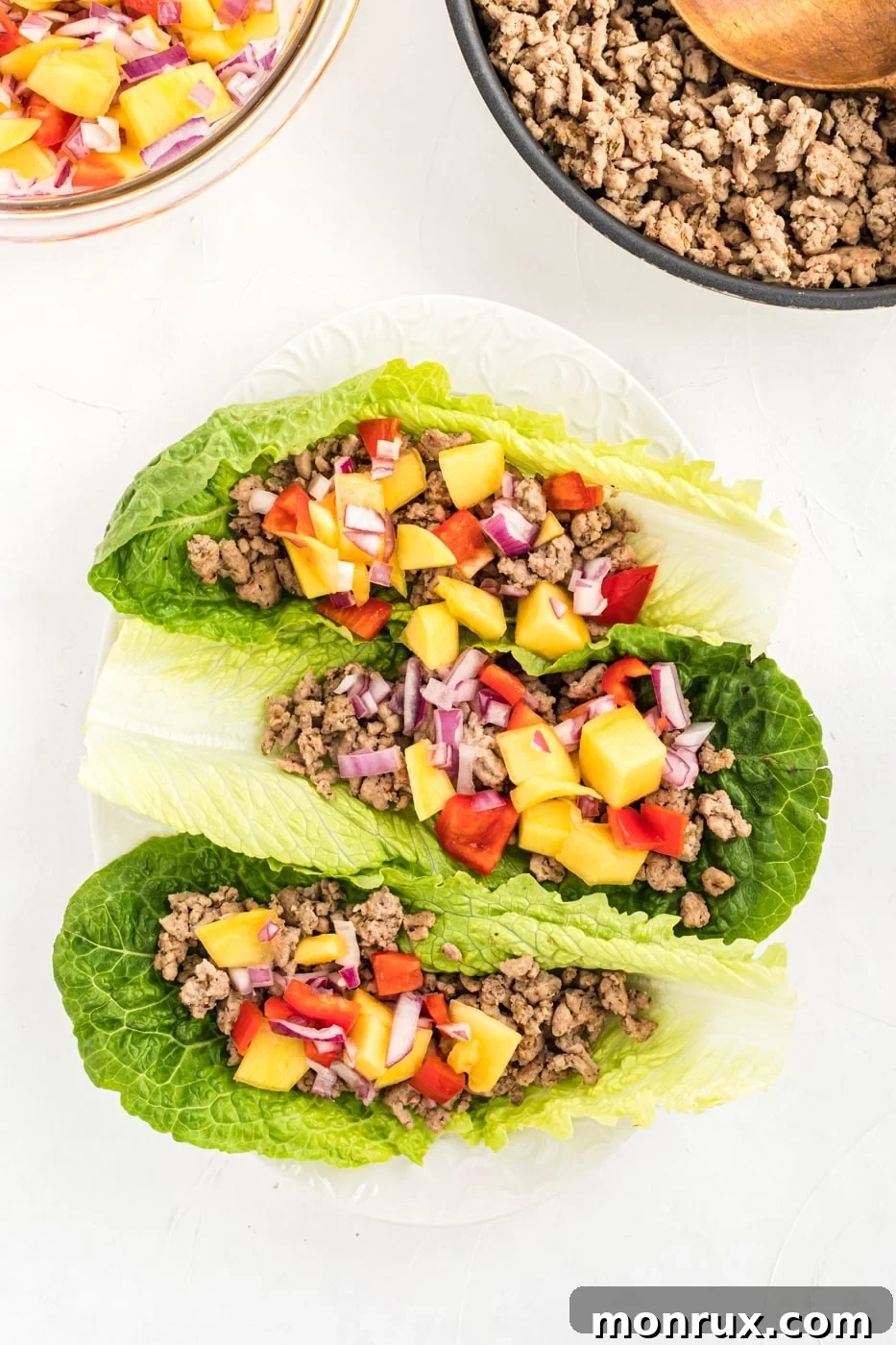 Ground chicken lettuce tacos on a plate with fresh mango salsa and avocado slices. The vibrant colors highlight the healthy and delicious nature of the meal.