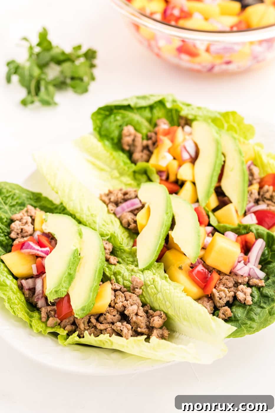 Ground chicken lettuce tacos with mango salsa and avocado, beautifully arranged on a white plate, highlighting a healthy and vibrant meal.