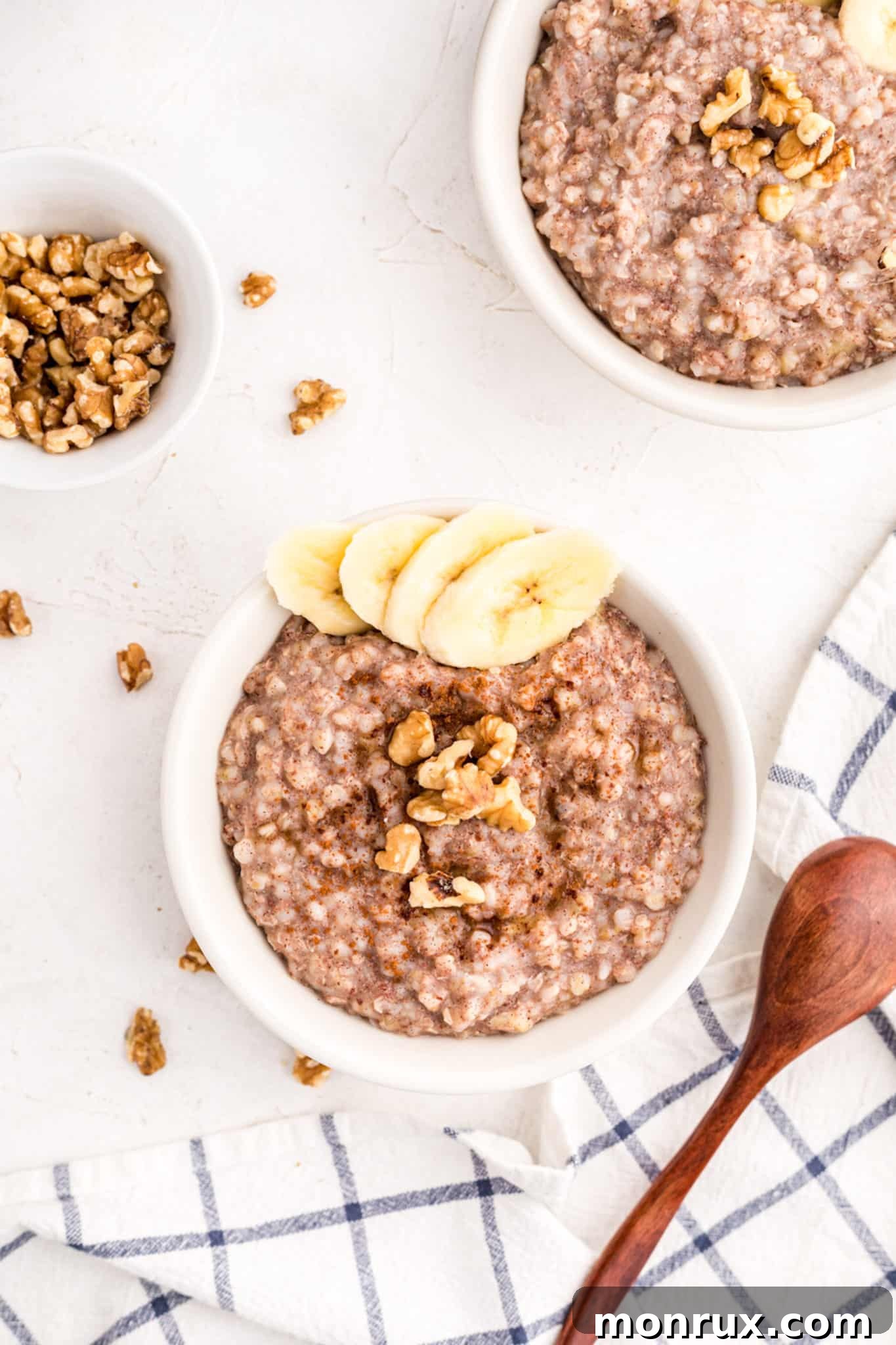 Two small bowls of buckwheat porridge topped with bananas and walnuts, with a spoon in one.