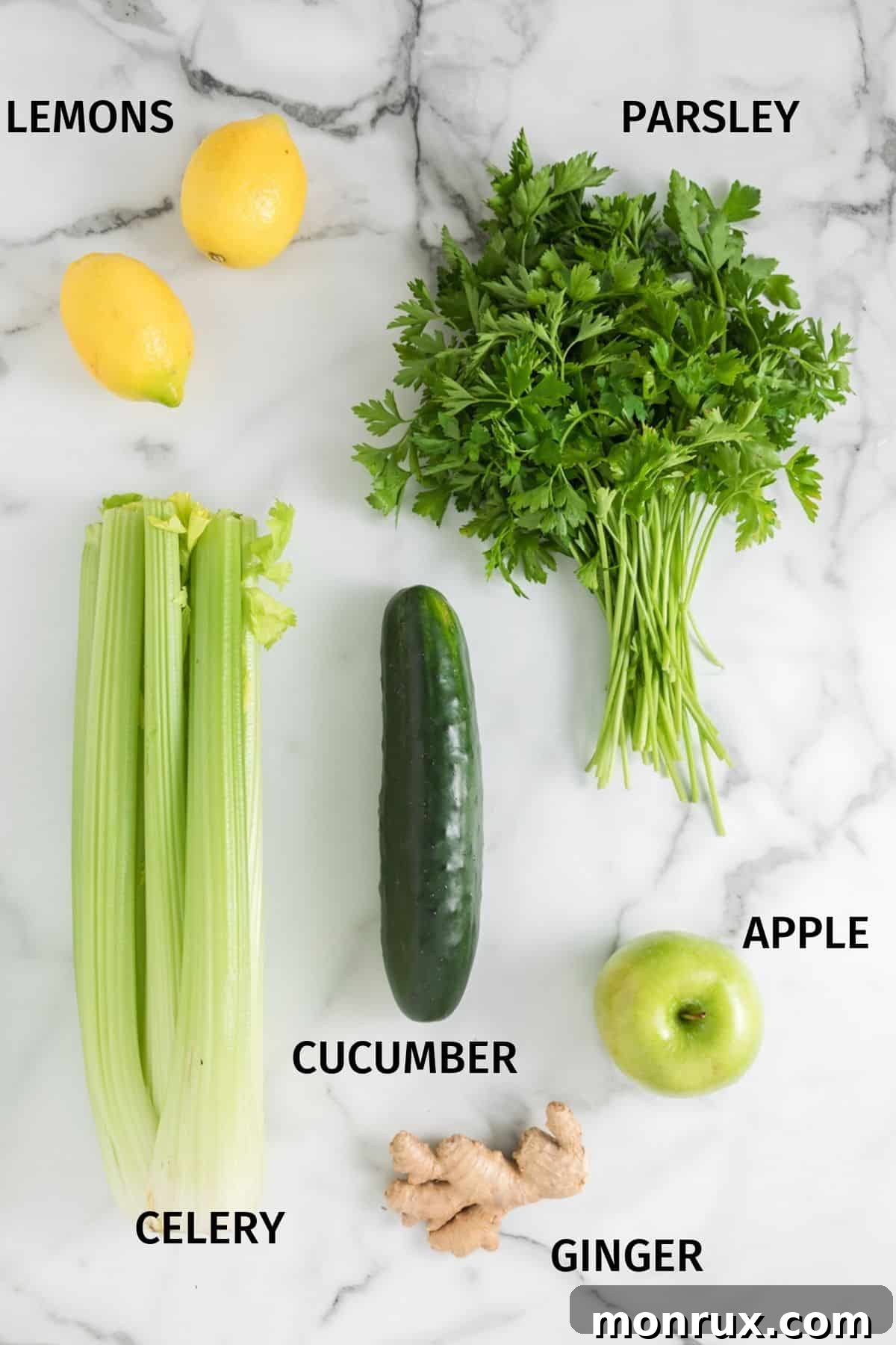 A collection of fresh green juice ingredients, including whole cucumbers, celery stalks, lemons, a green apple, fresh ginger root, and parsley, arranged on a white marble surface.