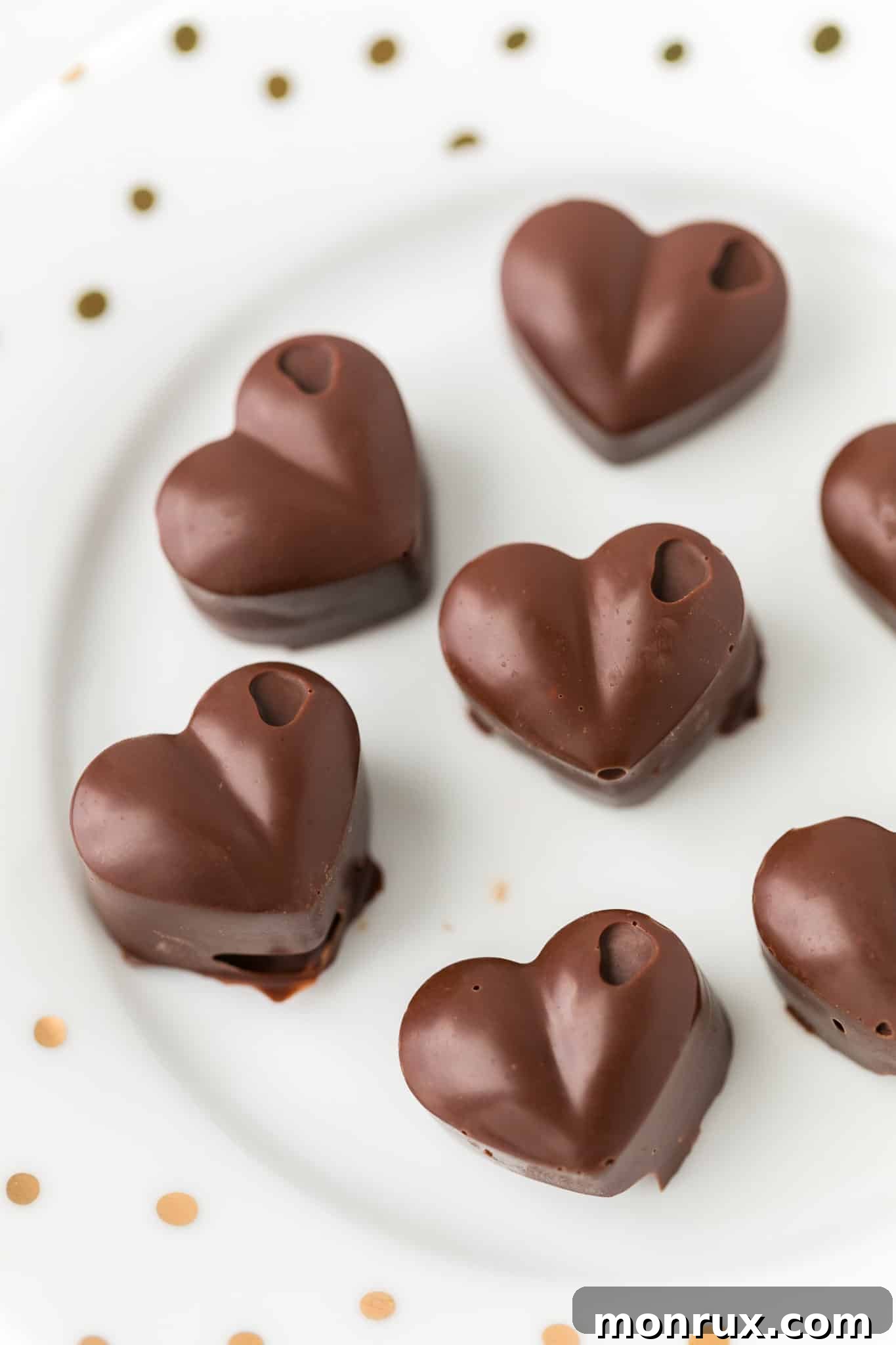 Homemade dark chocolate hearts adorned with a hint of raspberry flavor, served on a pristine white plate, perfect for Valentine's Day. The image shows several heart-shaped chocolates, some with a subtle glossy sheen.