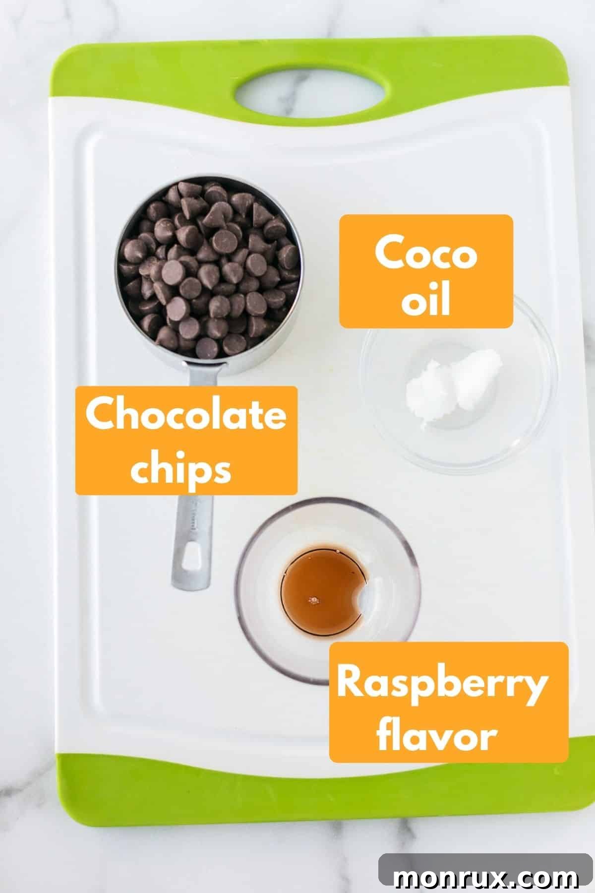 A close-up of the essential ingredients for chocolate raspberry hearts: a bowl of dark chocolate chips, a small jar of coconut oil, and a bottle of raspberry extract, arranged neatly on a surface.