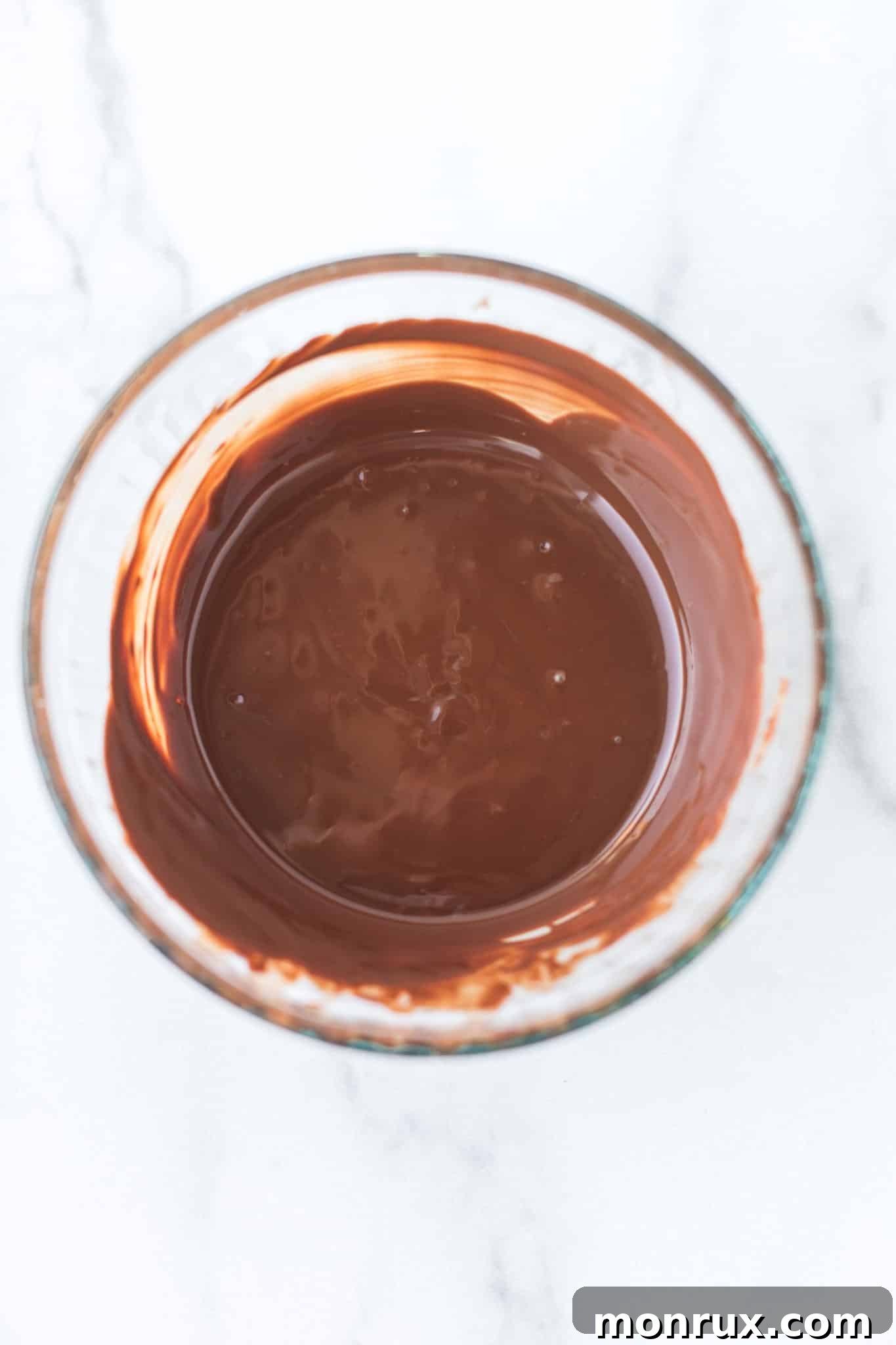 Smooth, glossy melted chocolate mixture in a transparent glass bowl, perfectly ready and waiting to be meticulously poured into the awaiting heart-shaped silicone molds.