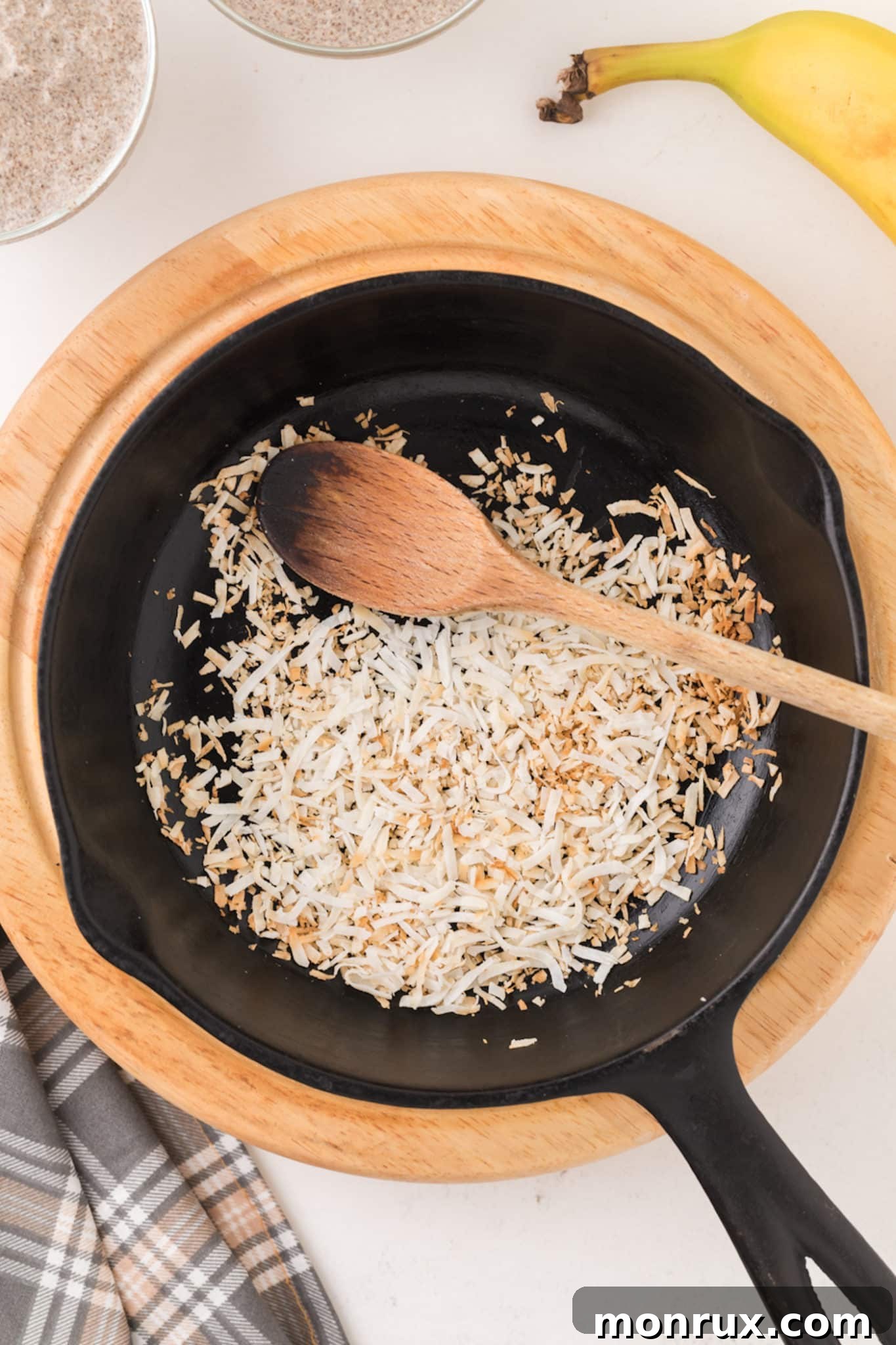 Unsweetened shredded coconut being toasted in a dry skillet over low heat, showing its transformation to a light brown color.