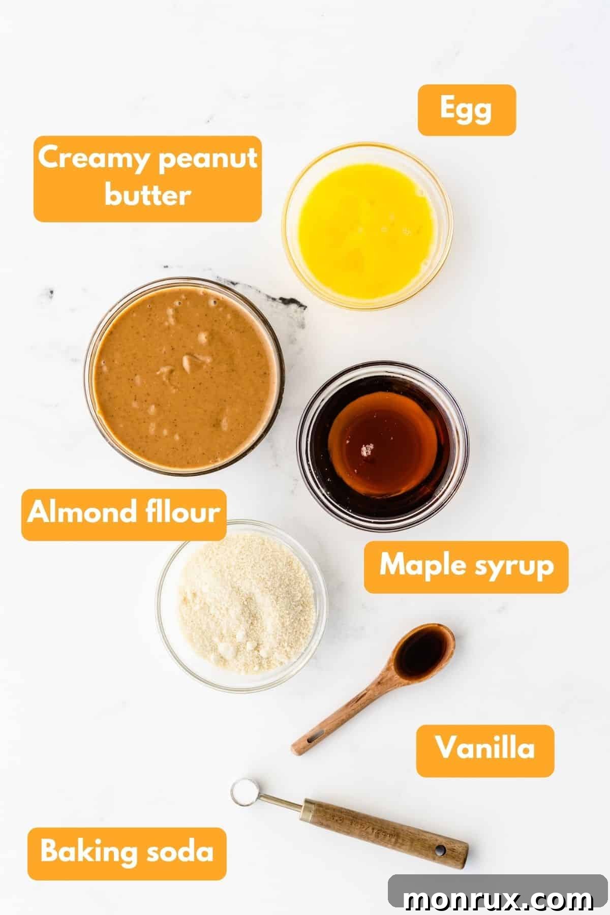 A collection of key ingredients for almond flour peanut butter cookies, including peanut butter, almond flour, maple syrup, and an egg.