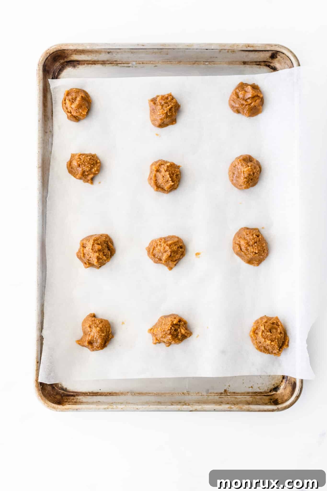 Uniform cookie dough balls neatly arranged on a parchment-lined baking tray.