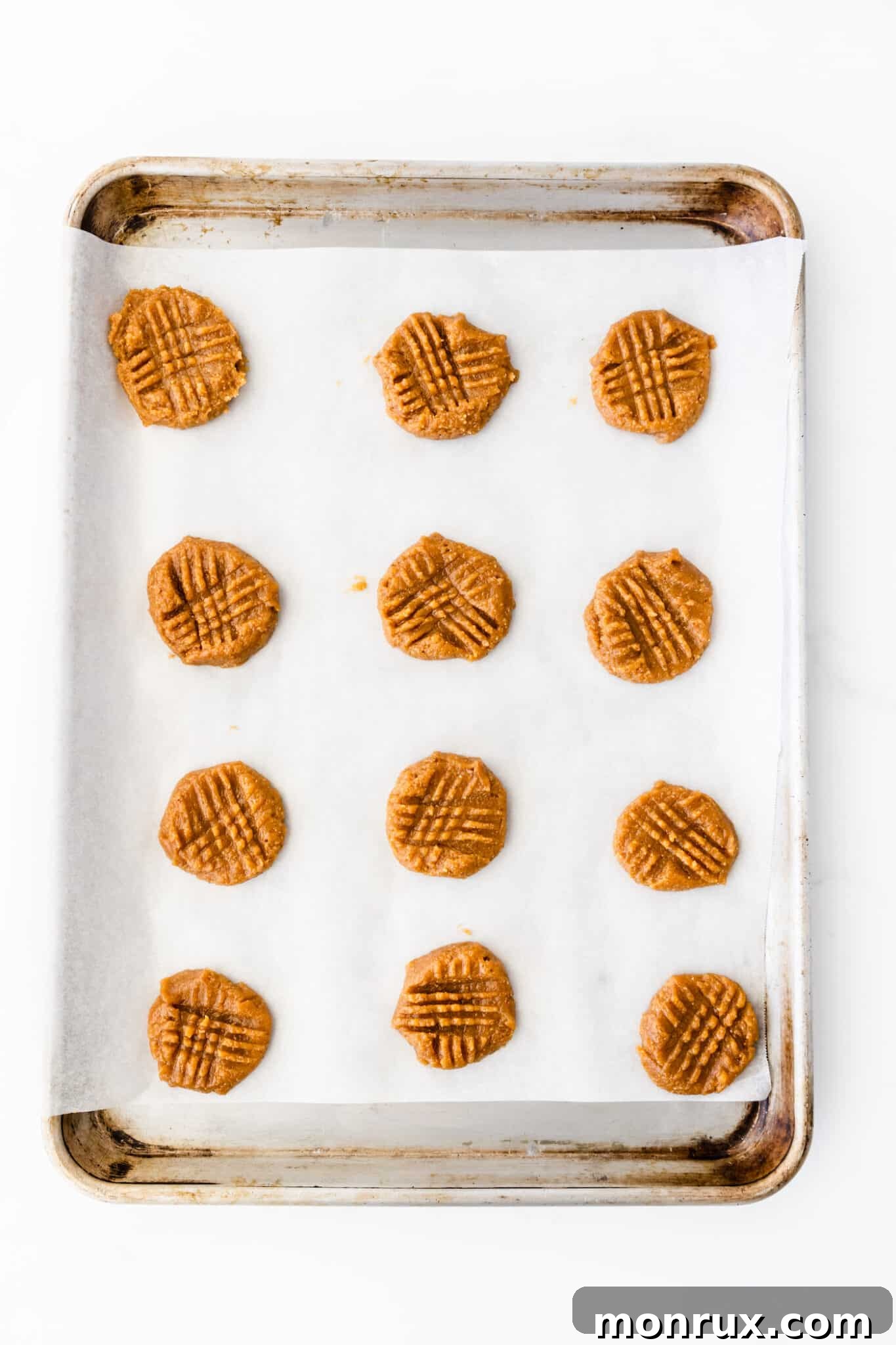 Flattened peanut butter cookies with characteristic crisscross fork marks, ready for baking.
