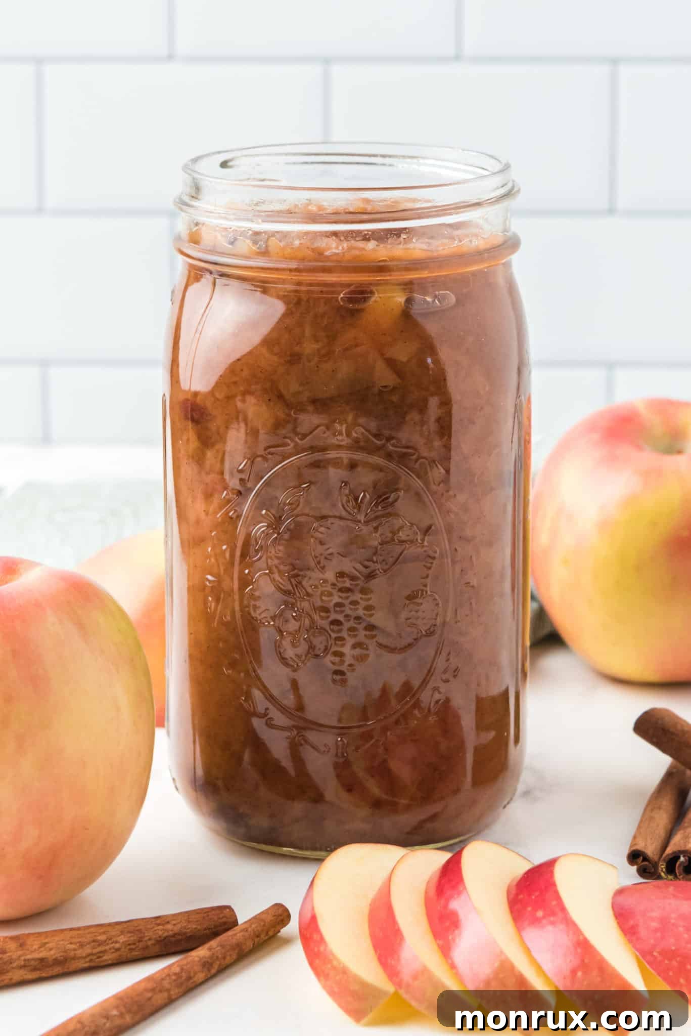 Jar of homemade crockpot applesauce on a rustic wooden table, garnished with a cinnamon stick.