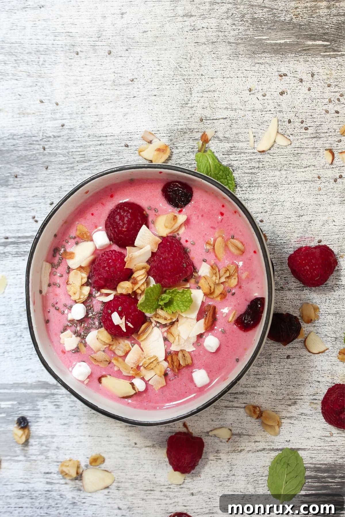 Smoothie bowl topped with fresh raspberries, crunchy granola, and shredded coconut.