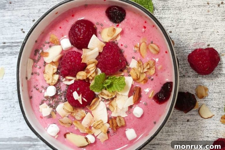 Creamy raspberry smoothie bowl garnished with fresh raspberries, granola, and shredded coconut.