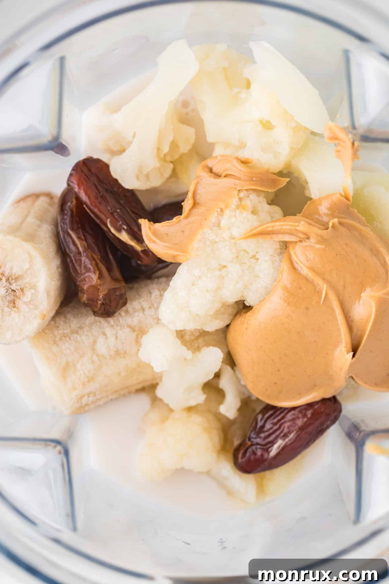 All smoothie ingredients, including frozen cauliflower, banana, peanut butter, and almond milk, placed in a high-speed blender, ready for blending.